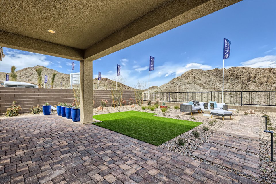 A brick patio with a brick walkway and a covered area with a fence and a hill in the.