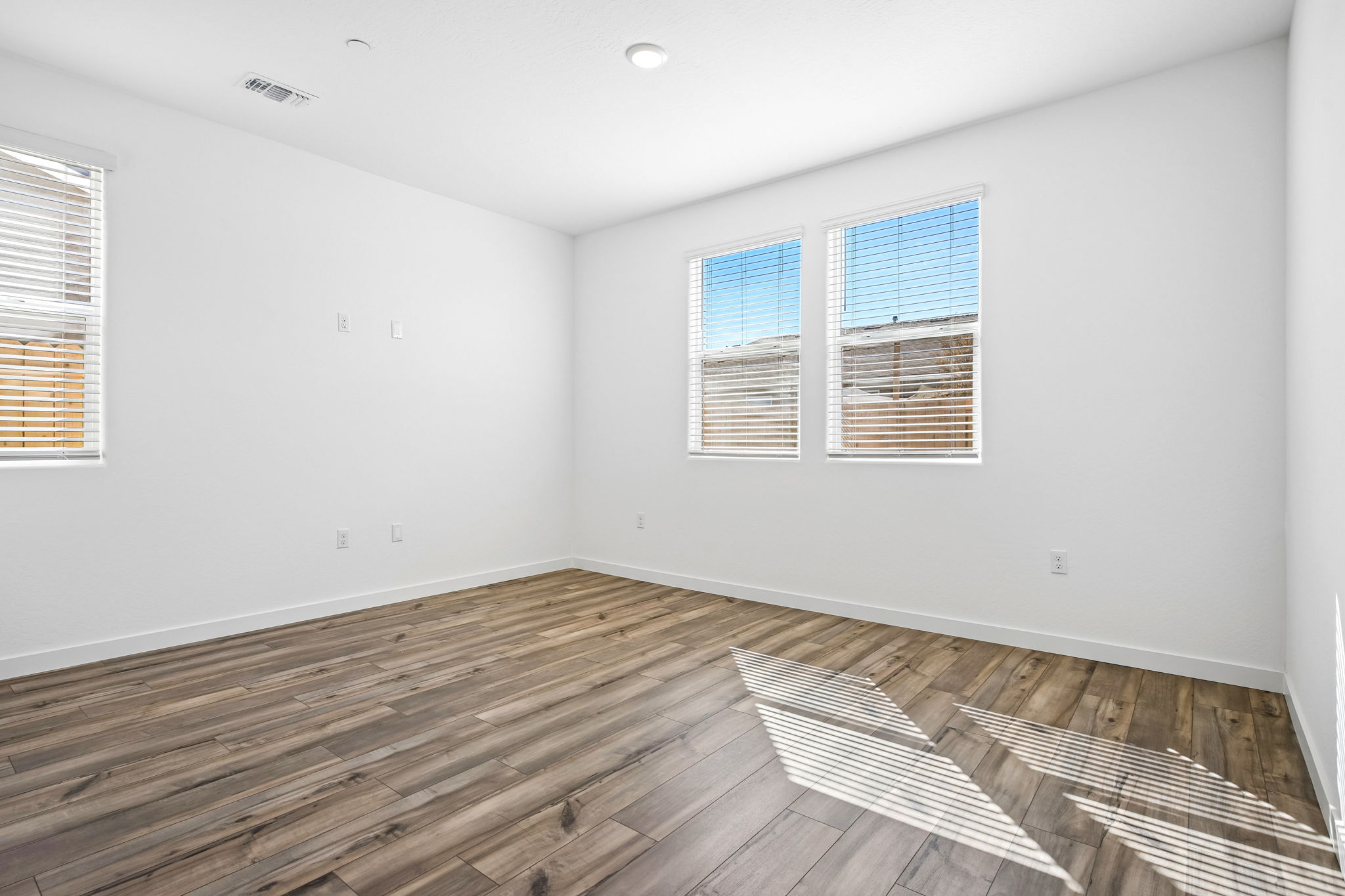 A room with a wood floor and a wood floor with a chair and a window with blinds.