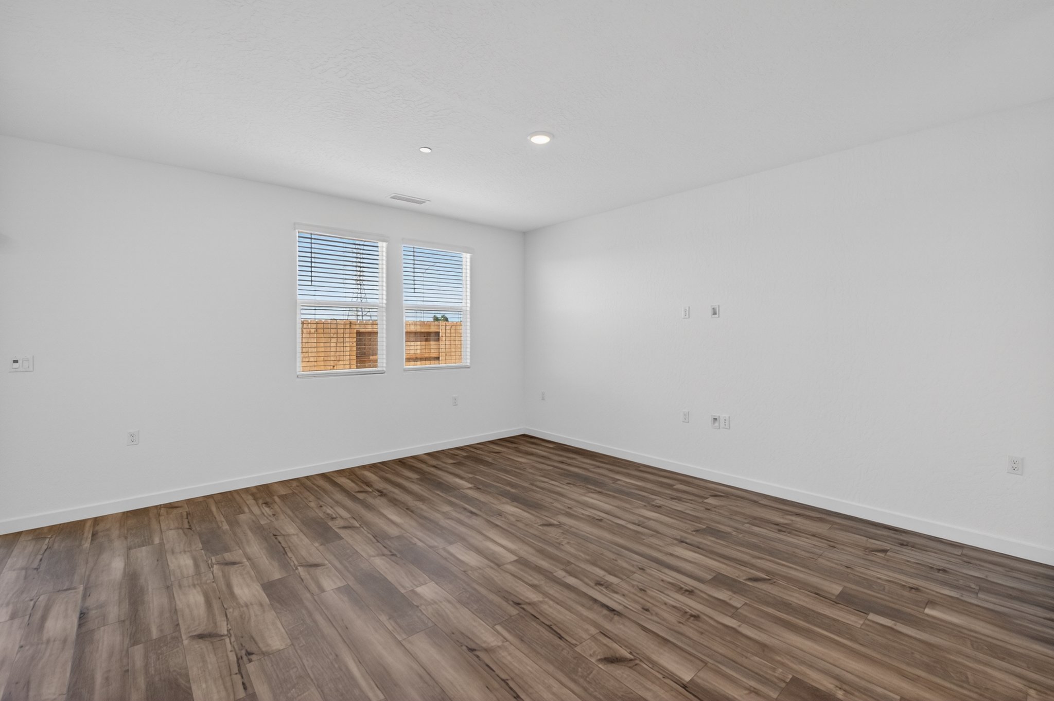 A room with a wood floor and a window with blinds.