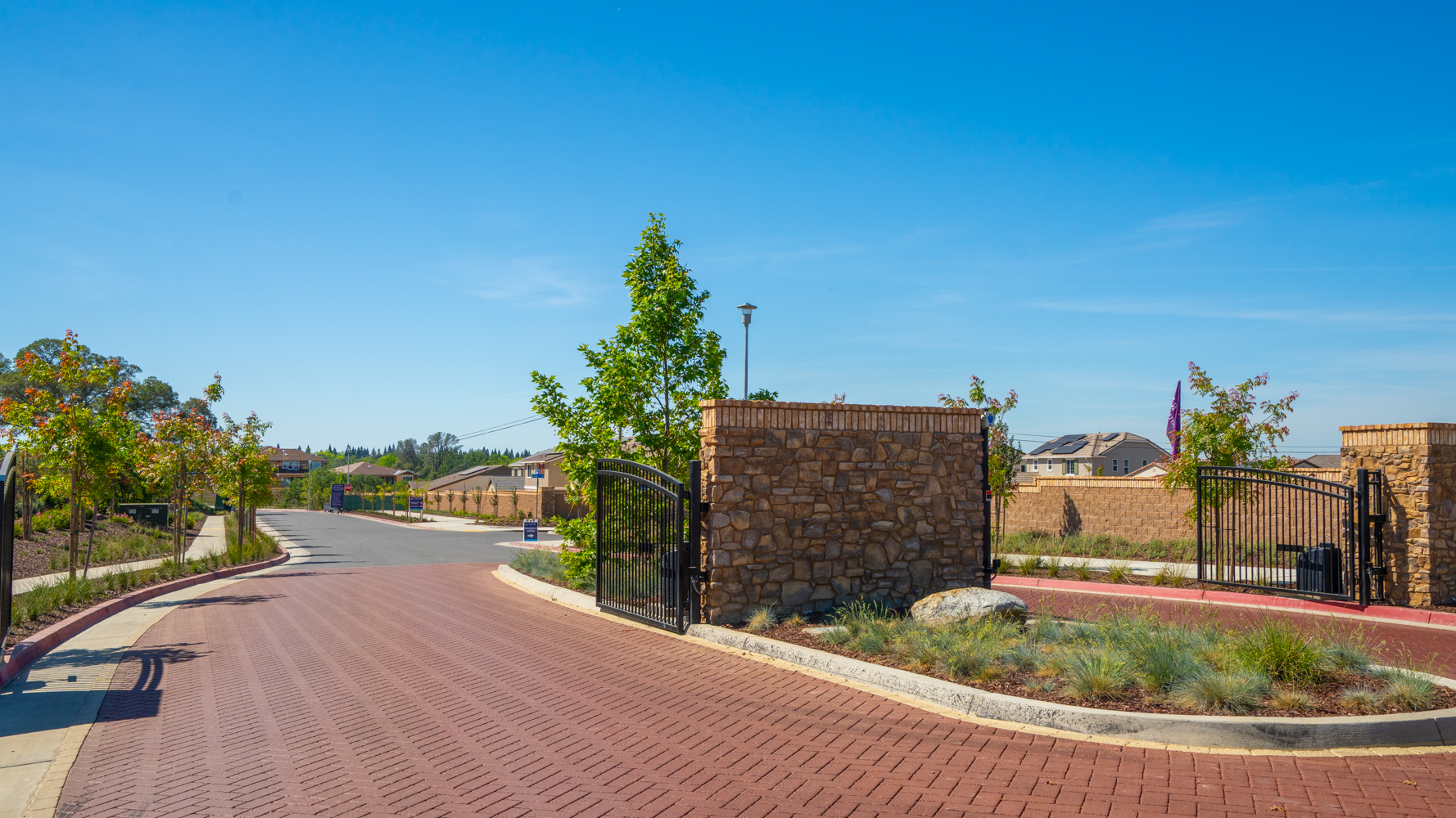 A brick road with a fence and trees on the side.