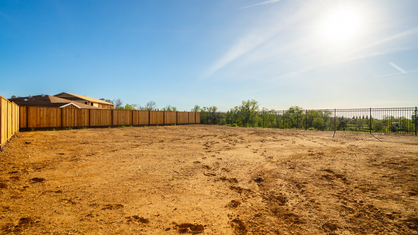 A dirt field with a fence and a building in the background.