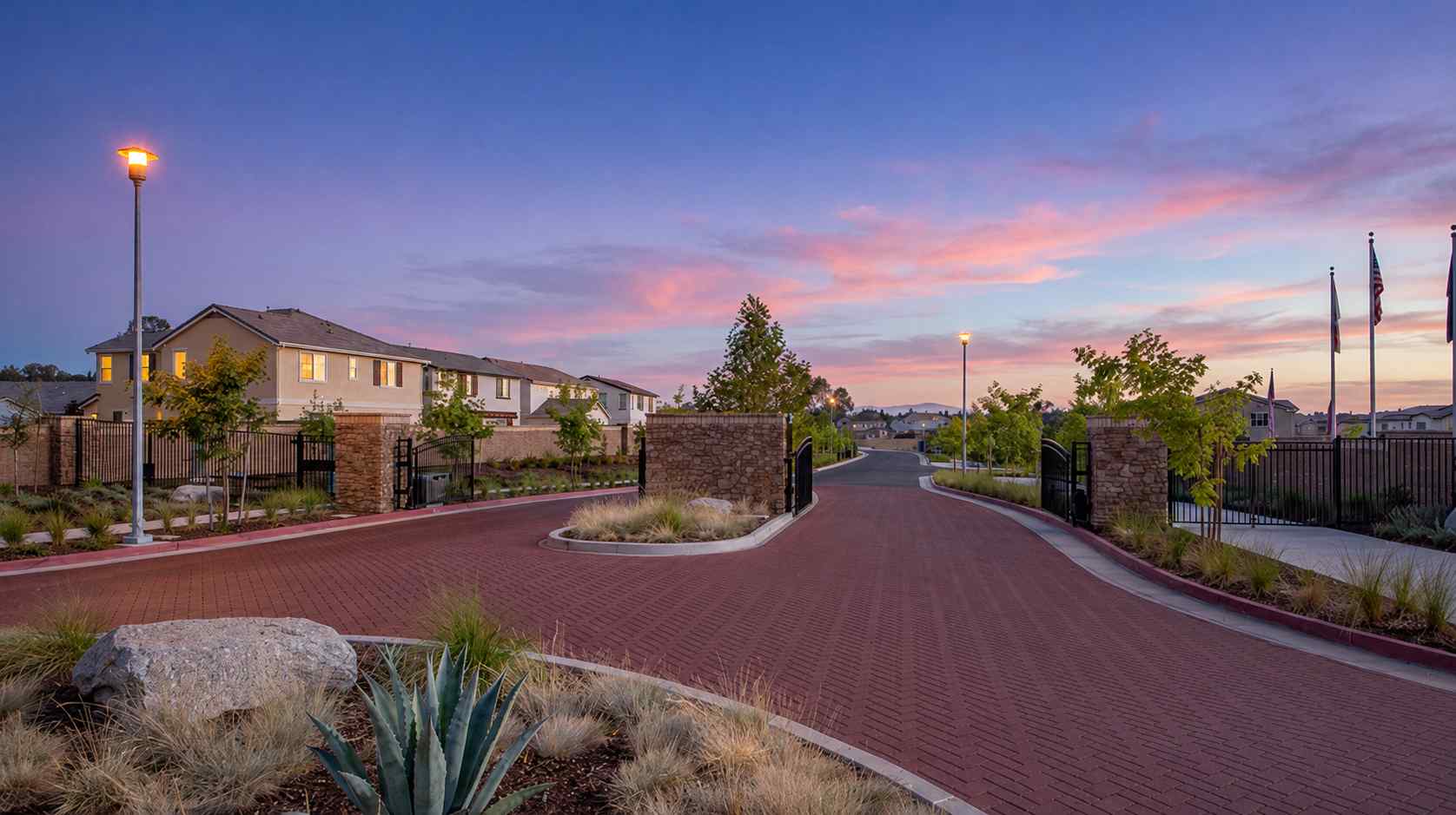 A brick road with a fence and trees on the side.