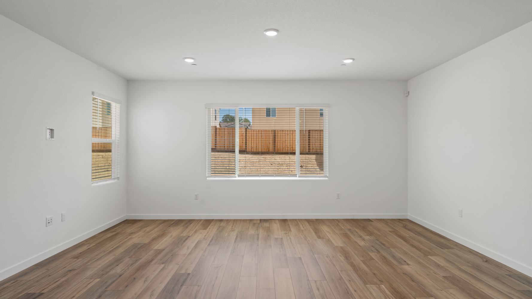A room with a wood floor and a window with blinds.