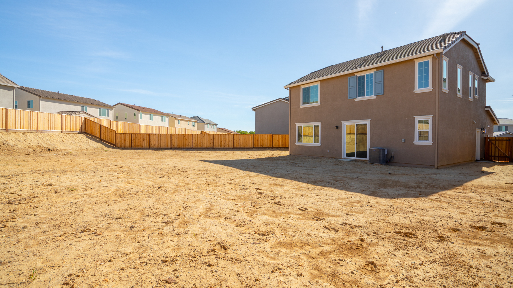 A dirt yard with a fence and a house in the background.