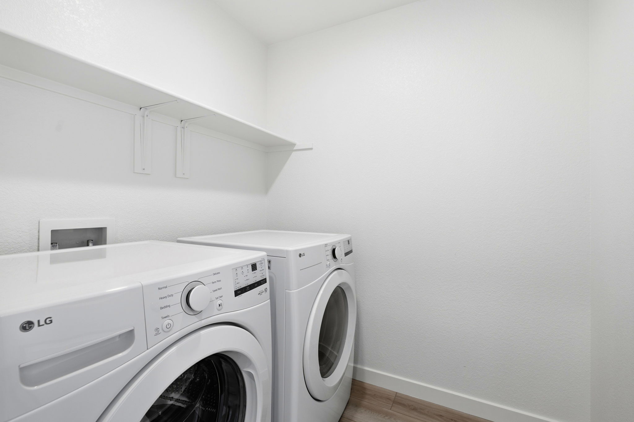 A white laundry room with a white wall and a white shelf.
