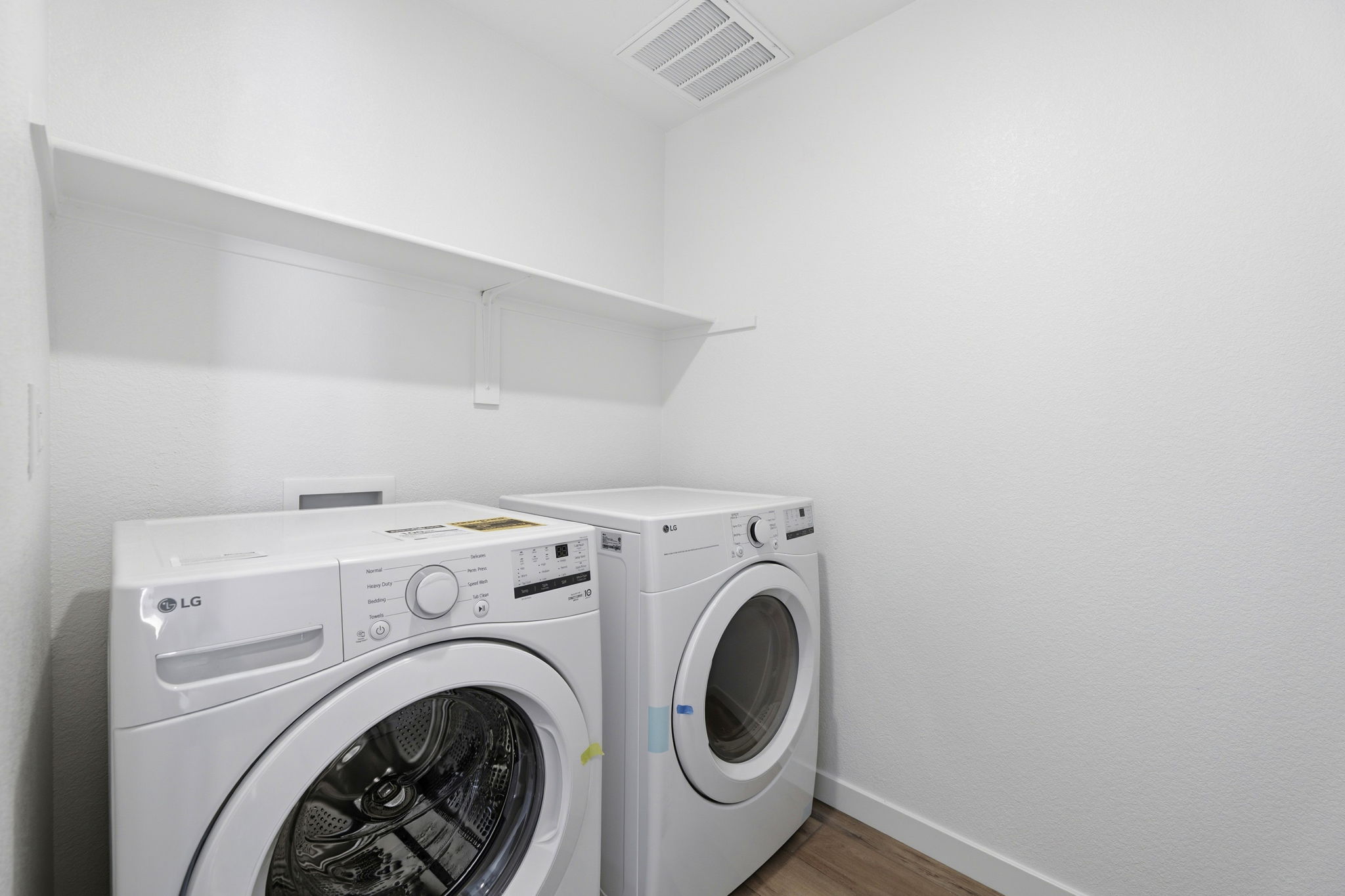 A white laundry room with a white laundry machine and white shelves.