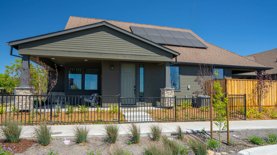 A house with a fence and bushes in front of it.