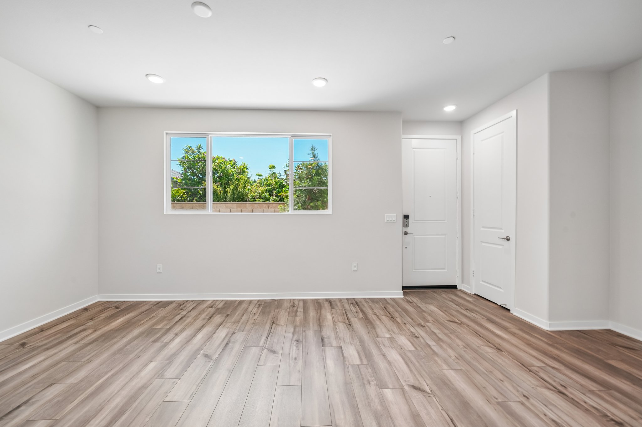 A room with a wood floor and a window with a view of trees.