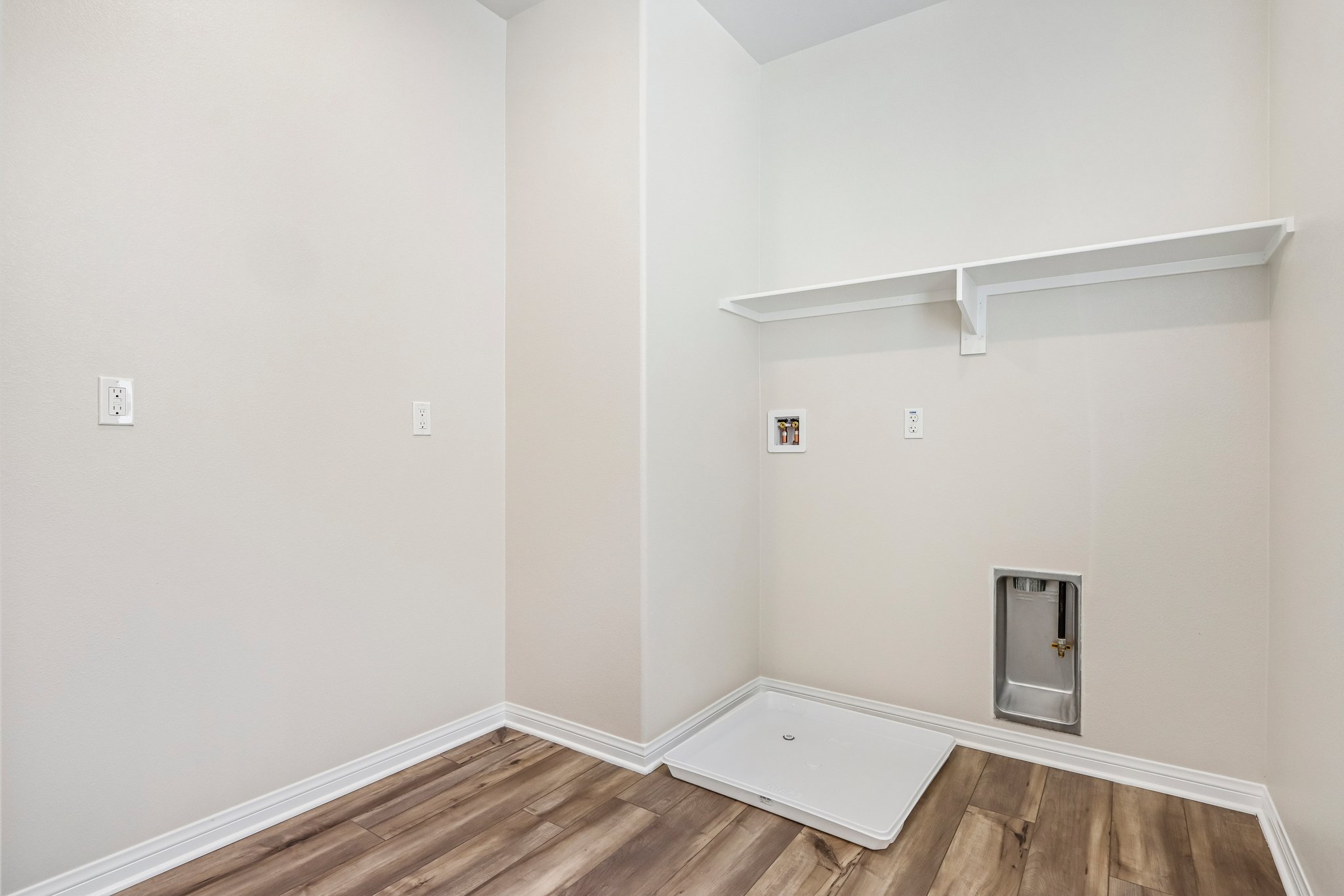 A room with a wood floor and a white wall with a vent.