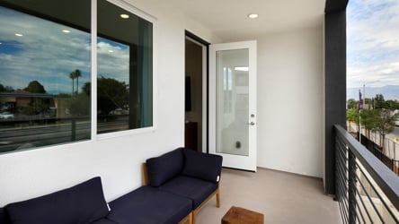 A room with a balcony and a patio with a couch and a table.