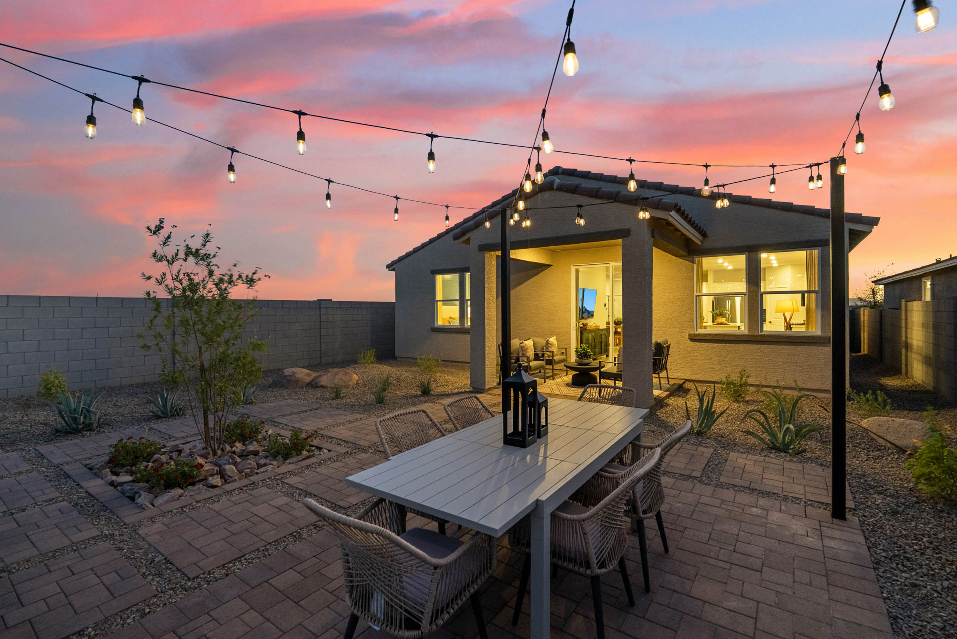 A patio with a table and chairs and a house with lights.