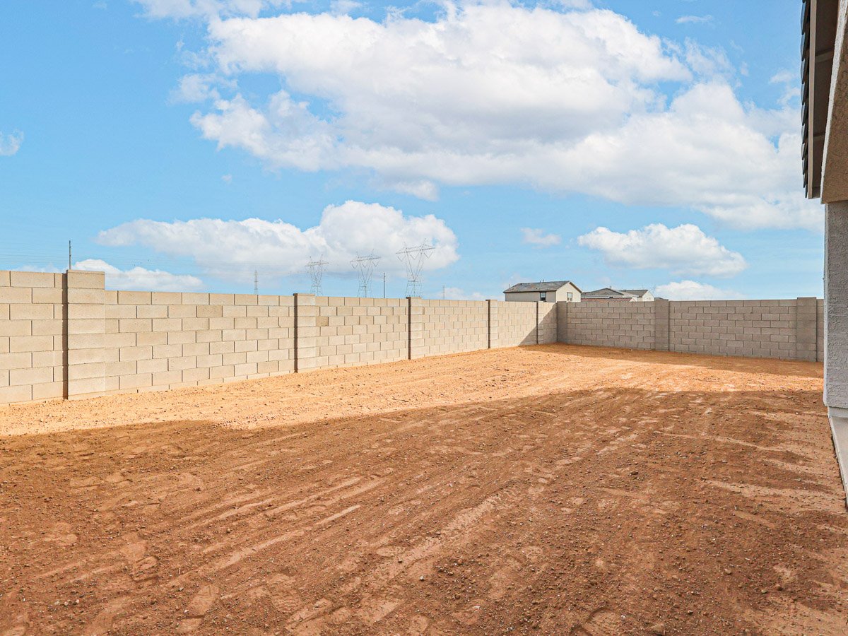 A dirt field with a fence and a building in the background.