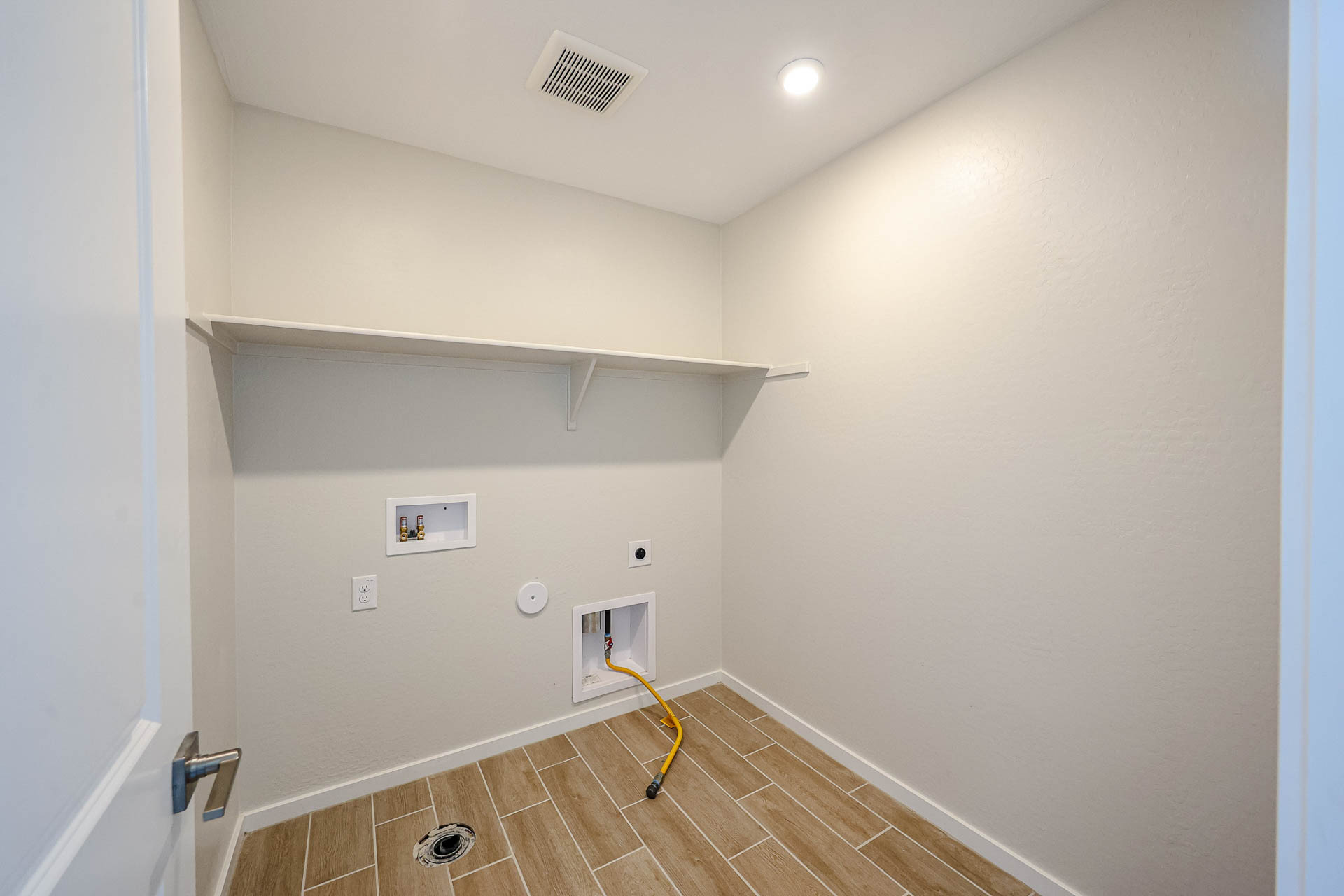 A room with a tile floor and a white wall with a yellow hose.