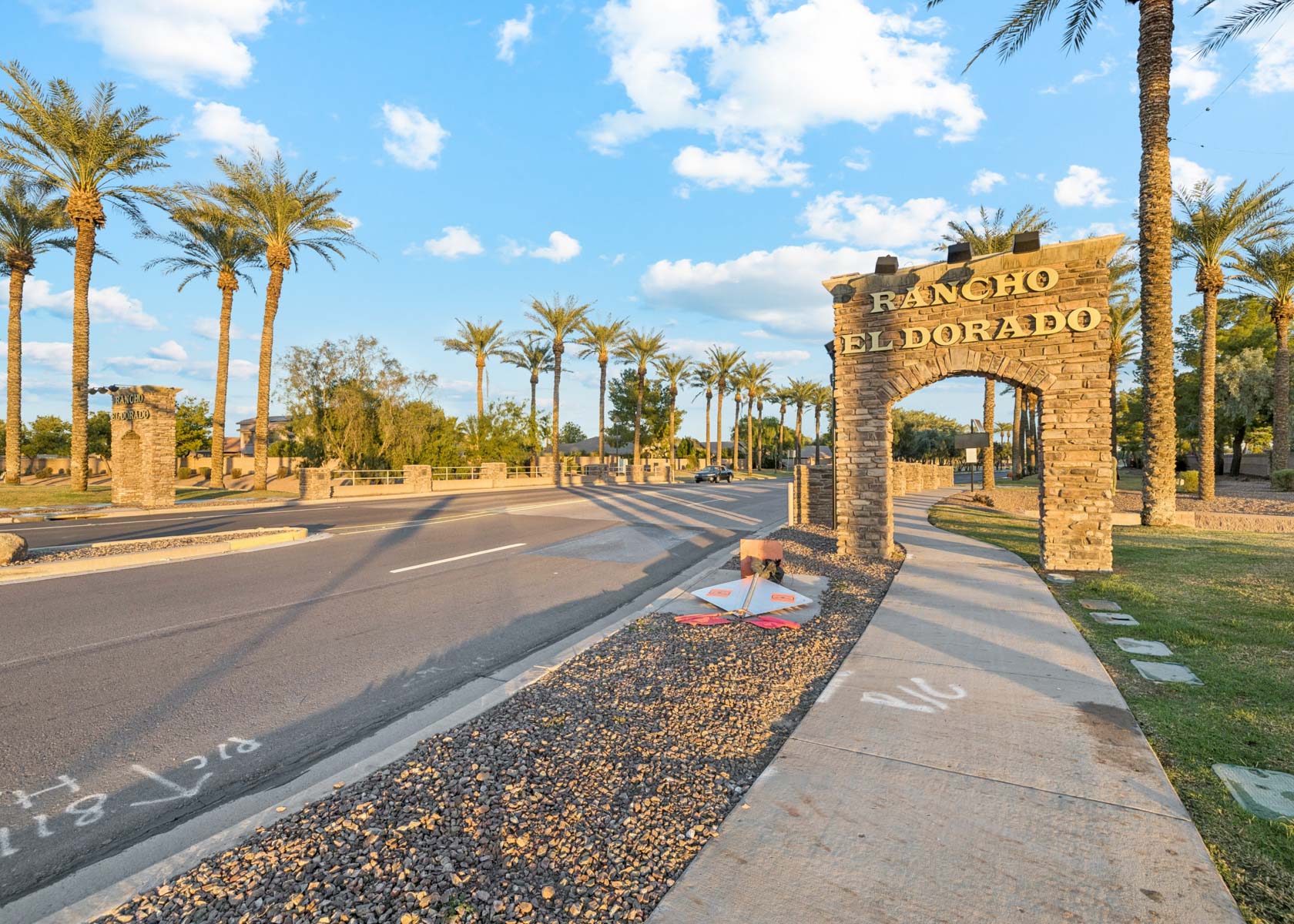 A road with palm trees and a stone archway.