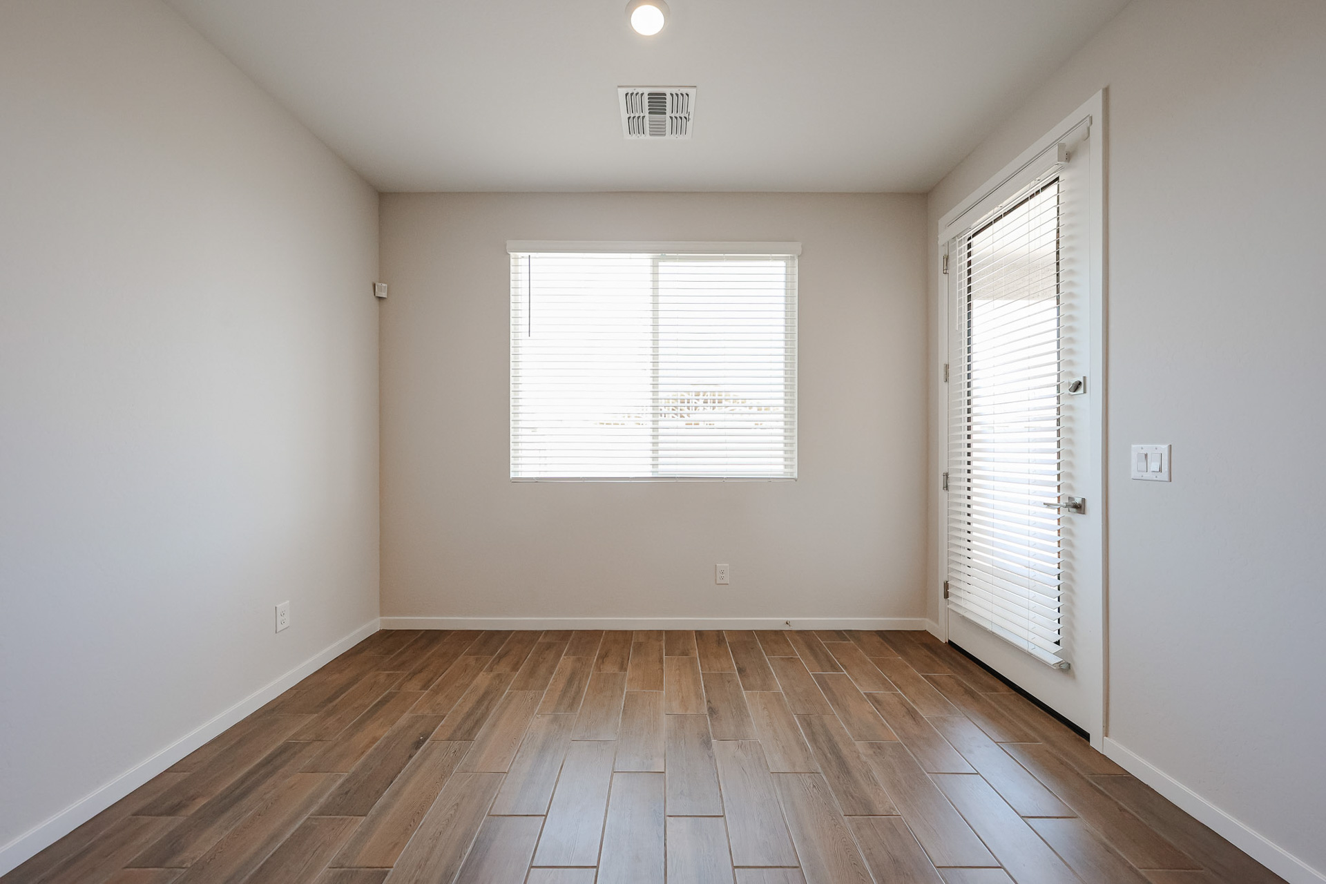 A room with a wood floor and a window with blinds.