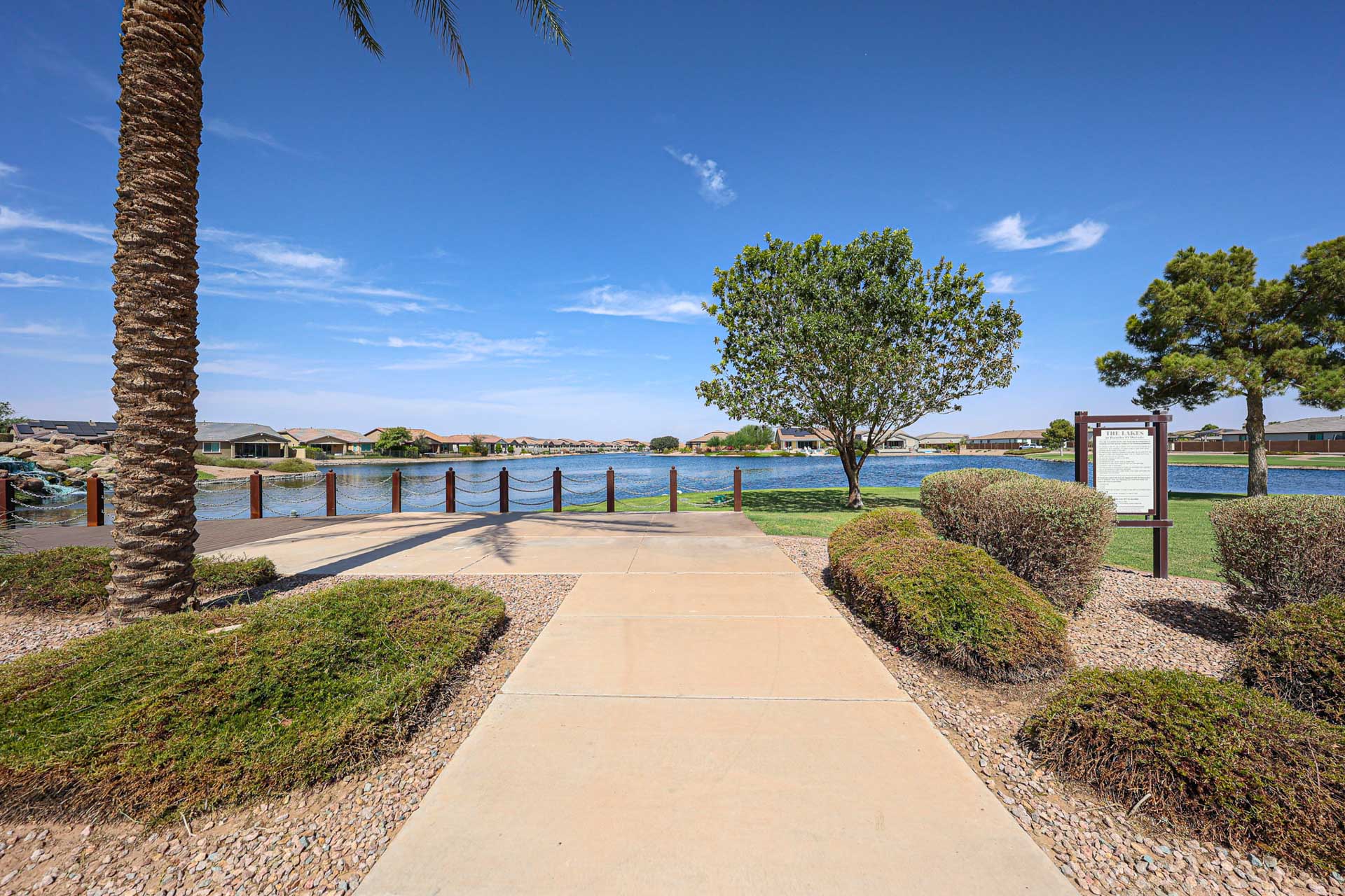 A walkway with trees and bushes by a body of water.