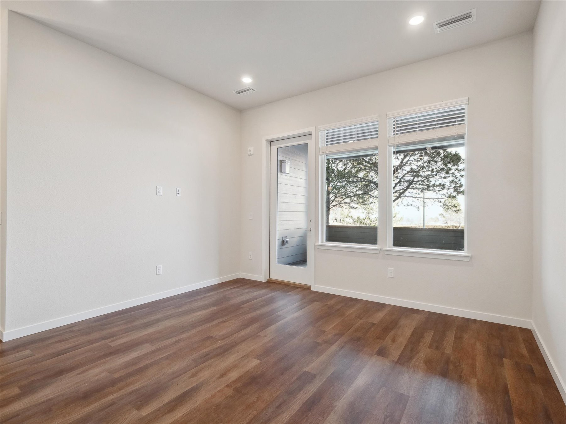 A room with a wood floor and a window with blinds.