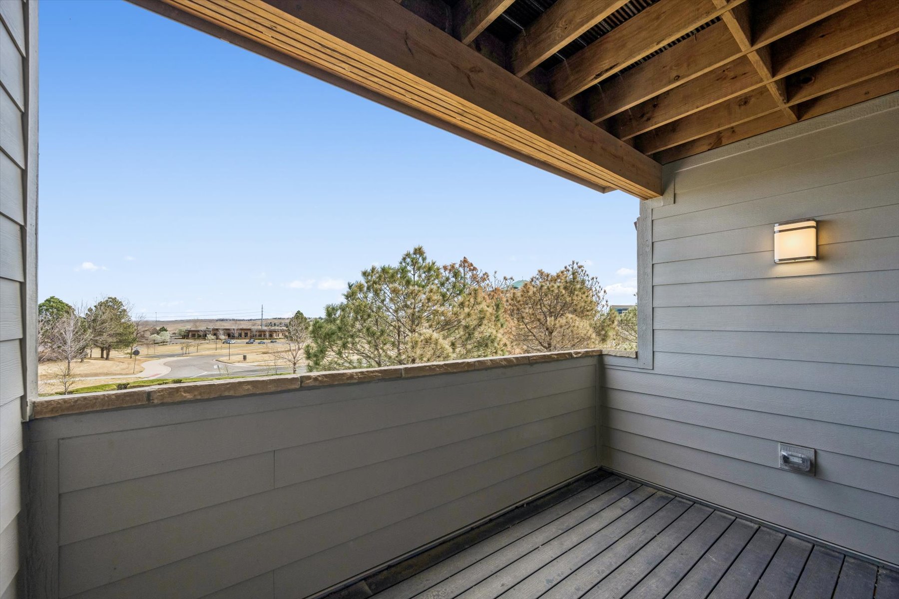 A deck with a wood railing and a tree and blue sky.