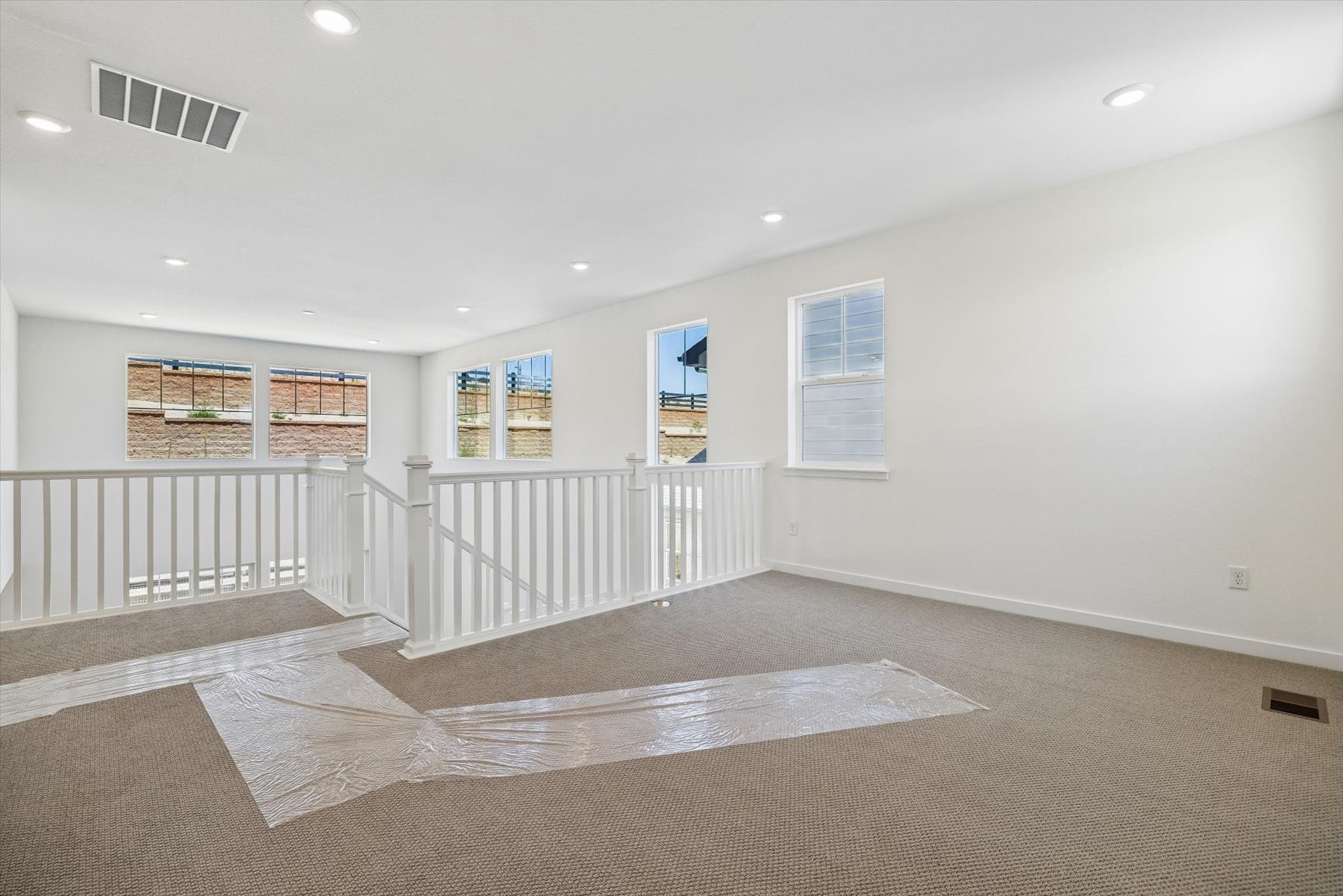 A large empty room with a white railing and a rug.