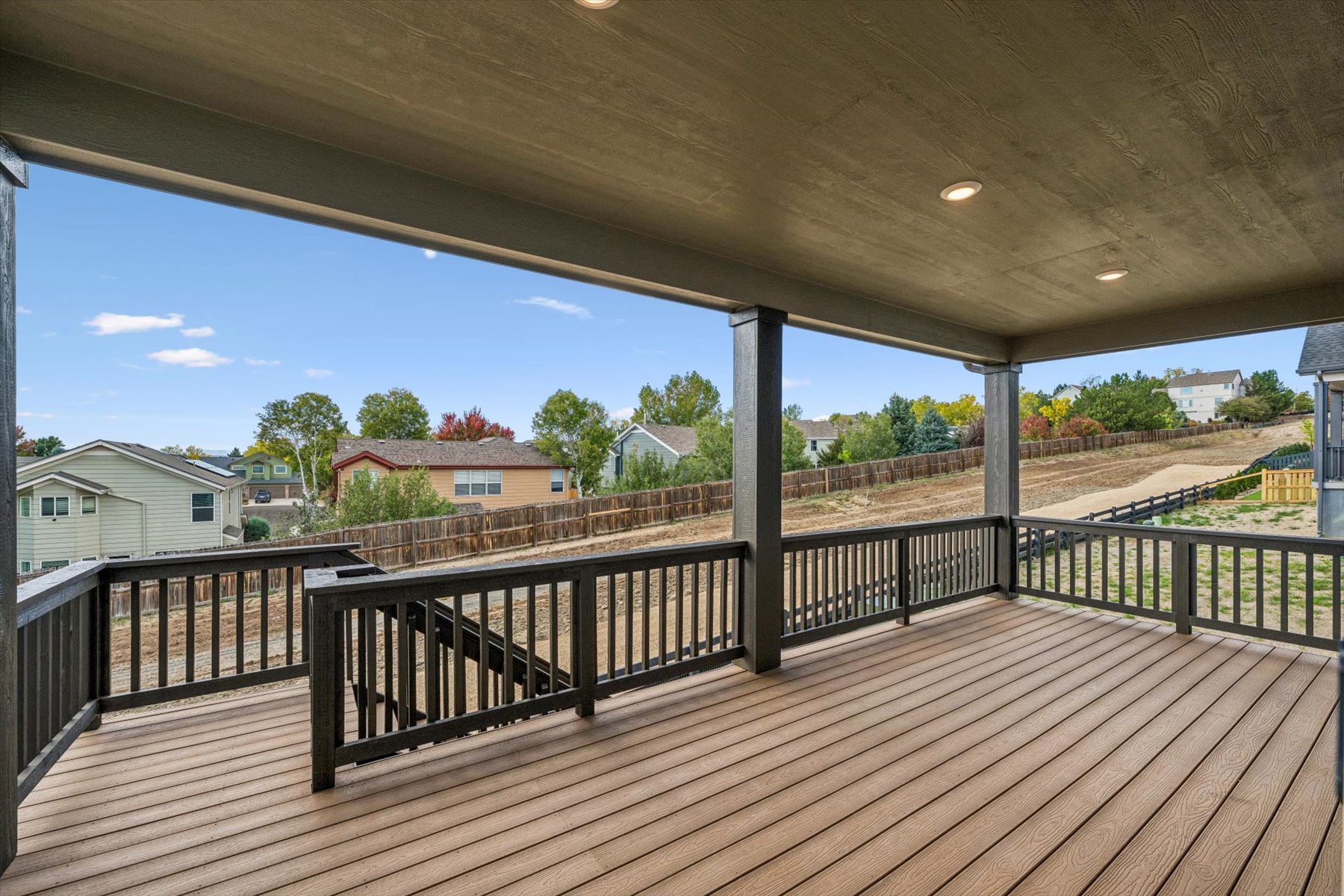 A deck with a railing and a view of a town and trees.