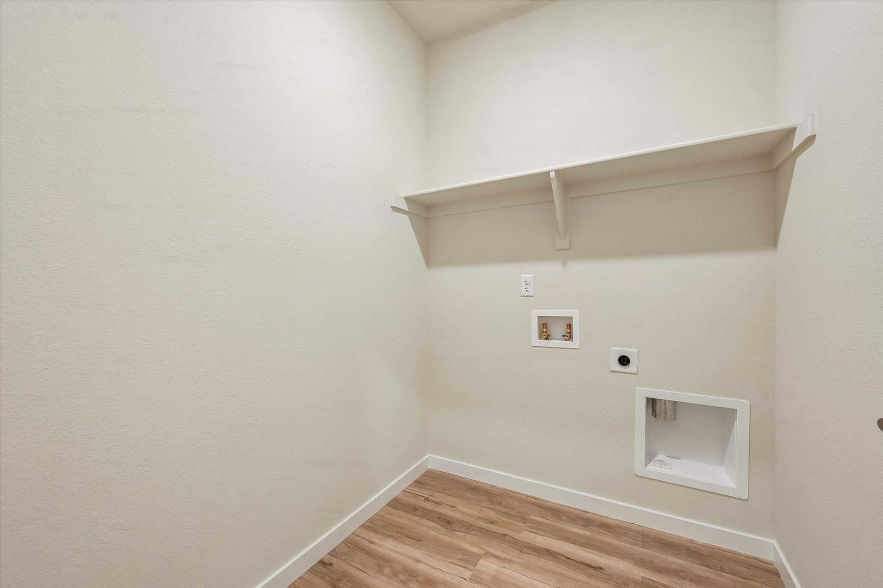 A white room with a wood floor and a white wall with a light.