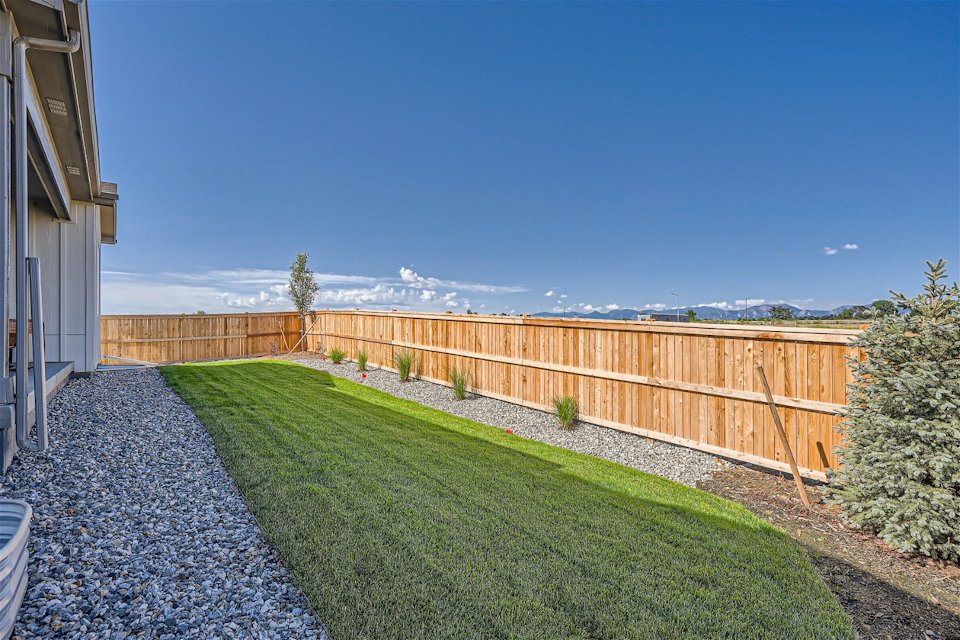 A fenced in yard with a tree and a building and blue sky.
