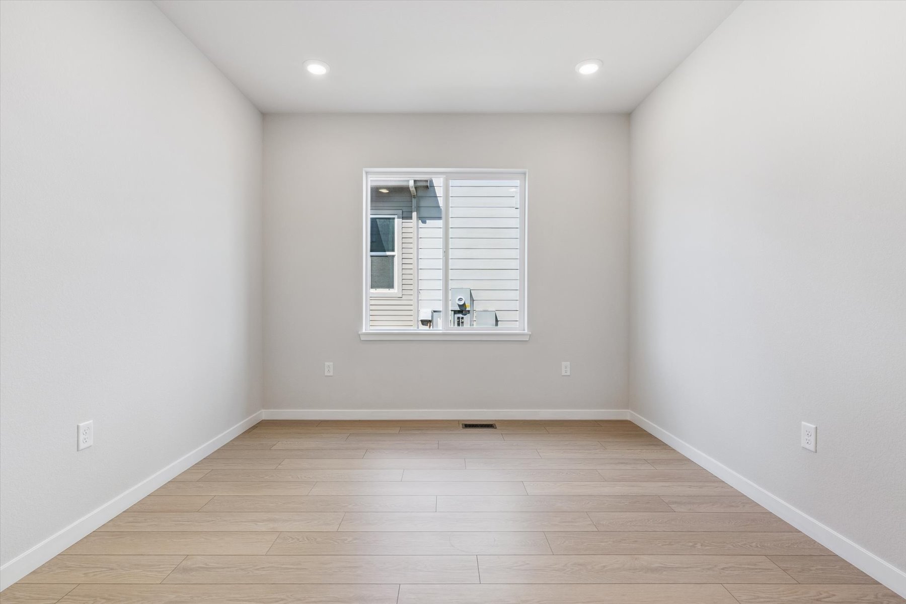 A room with a wood floor and a white wall with a window.