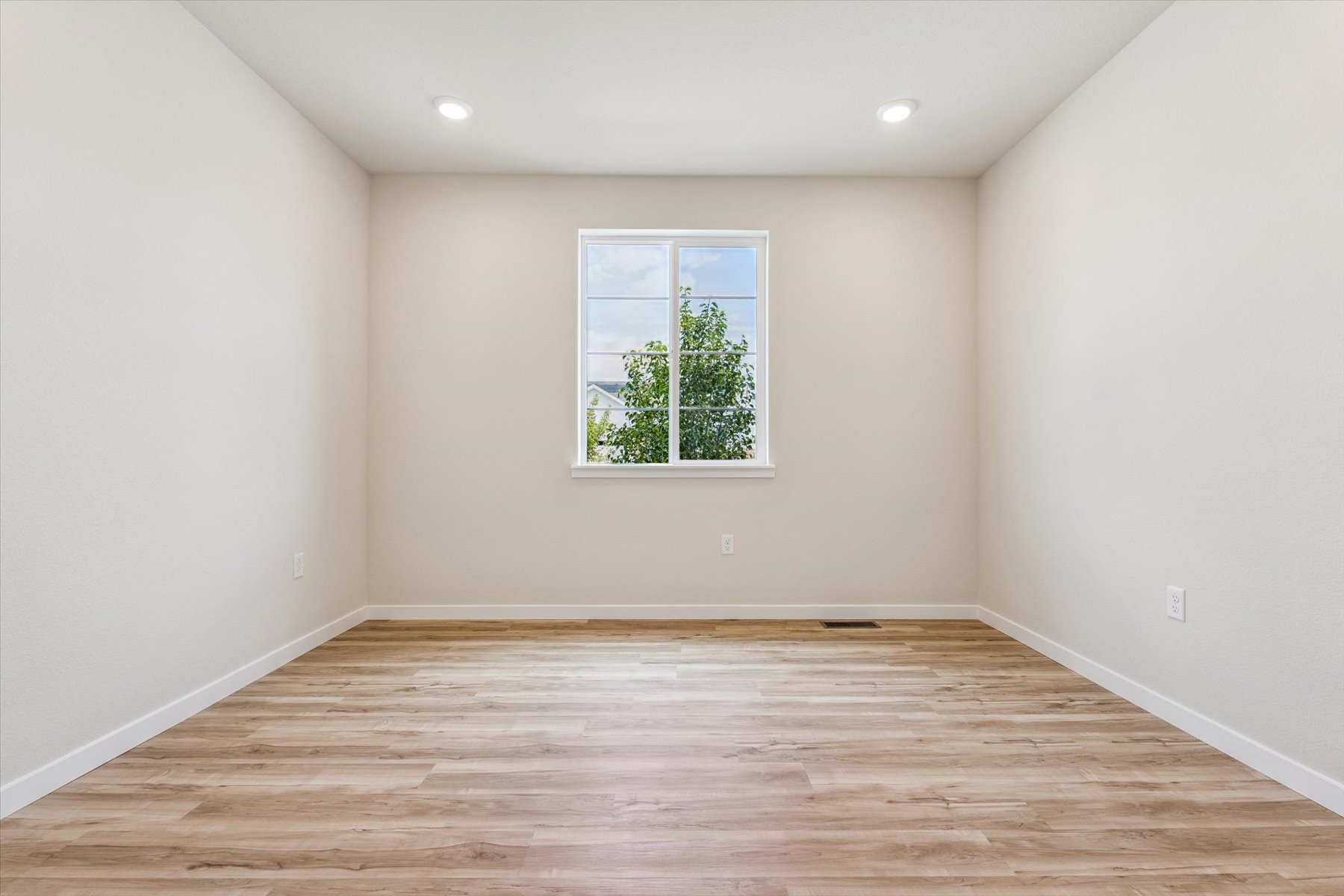 A room with a wood floor and a window with a tree outside.