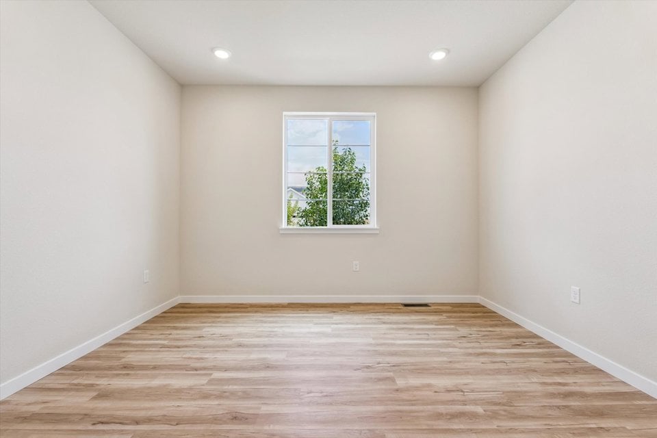 A room with a wood floor and a window with a tree outside.