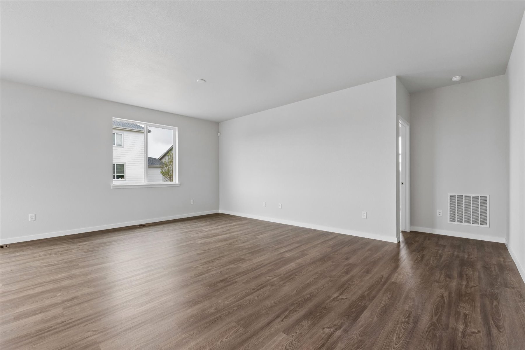 A room with a wood floor and a white wall with a window.