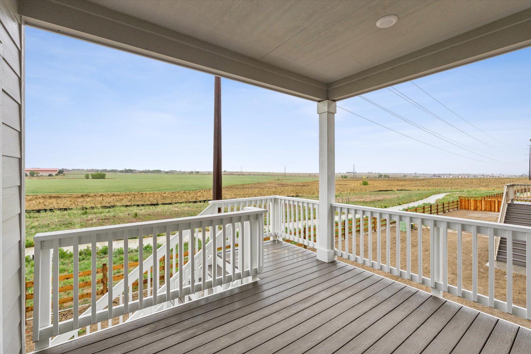 A wooden deck with a railing and grass and a field in the background.