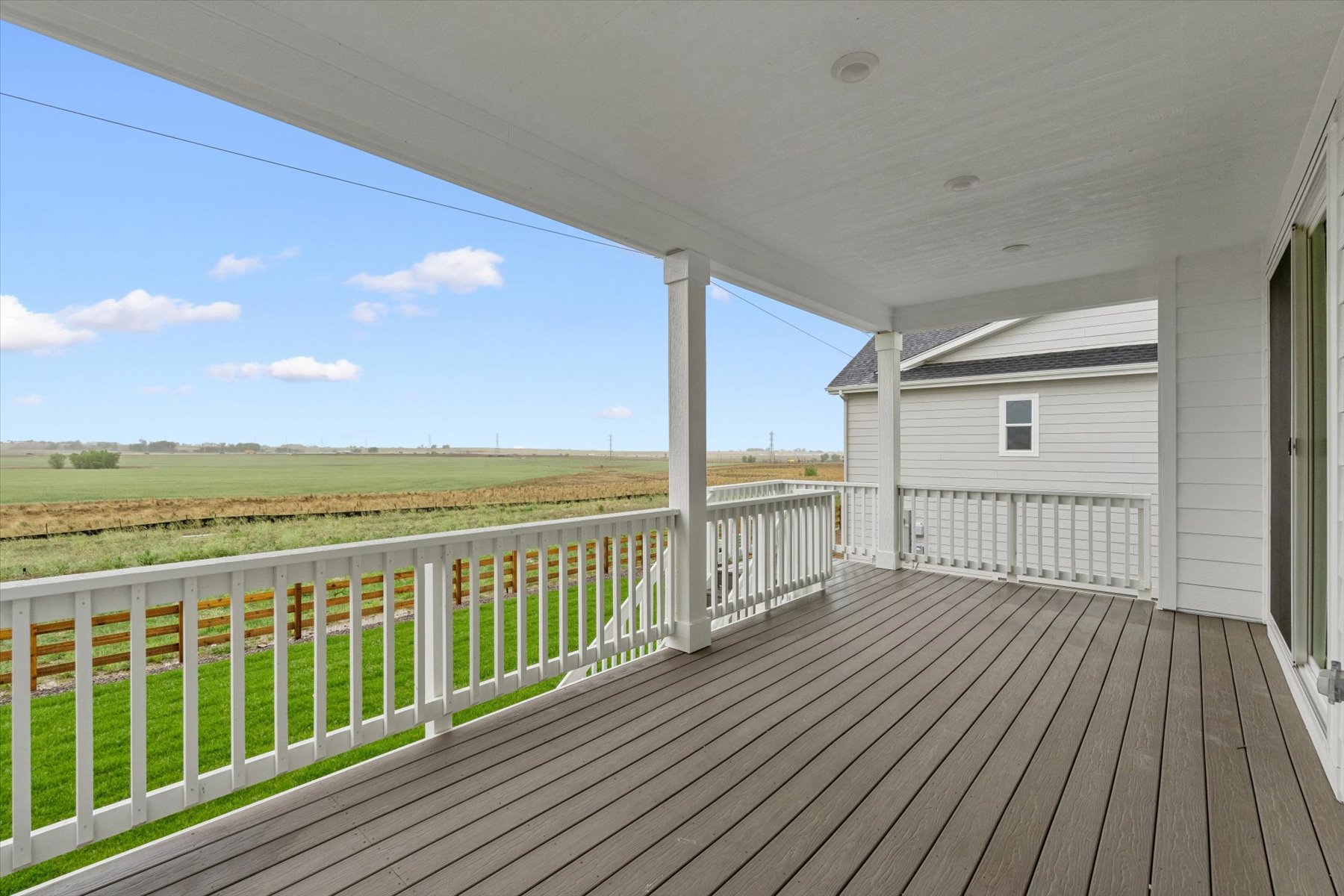 A wooden deck with a white fence and a white building with a field in the background.
