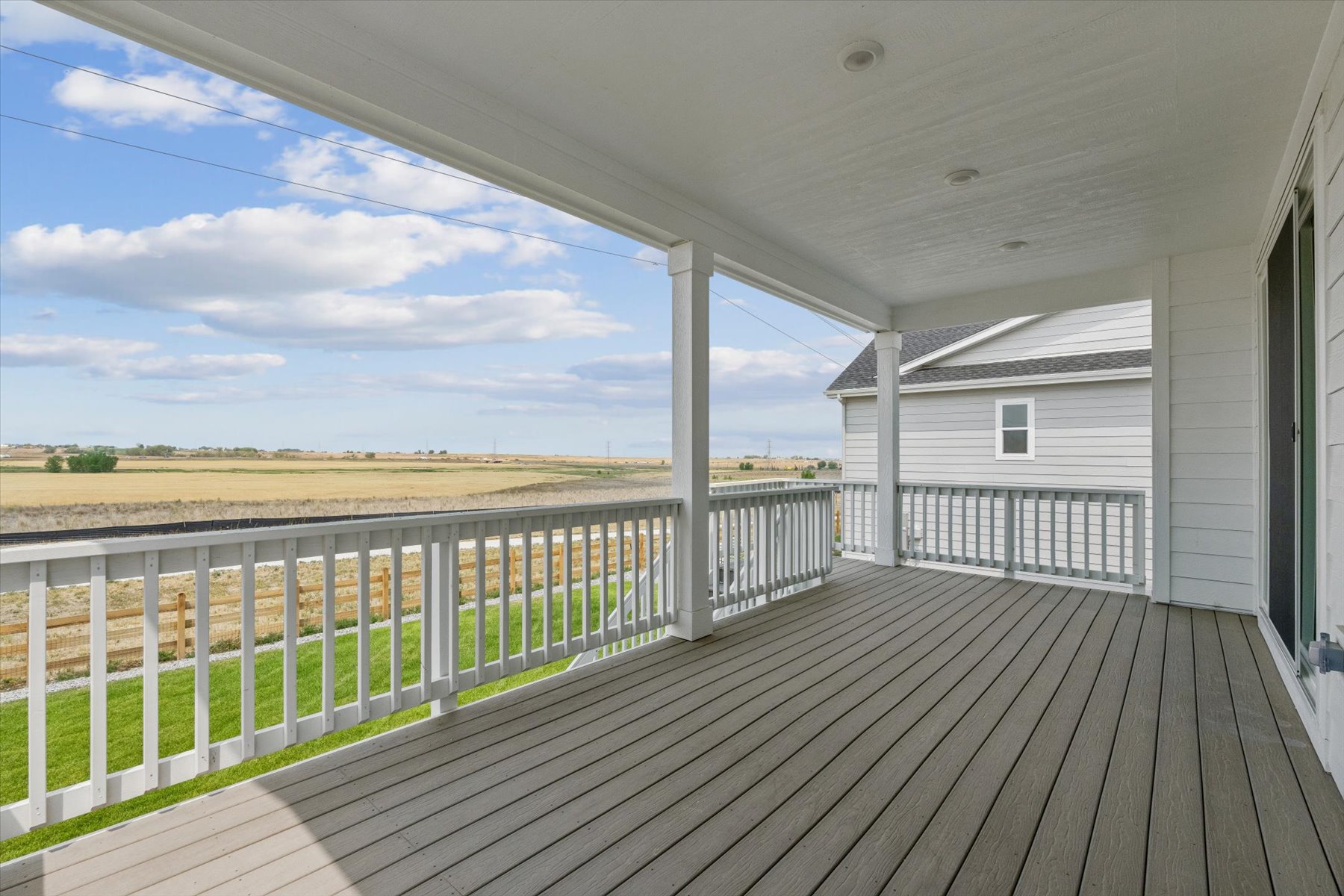A wooden deck with a white building and a field in the background.