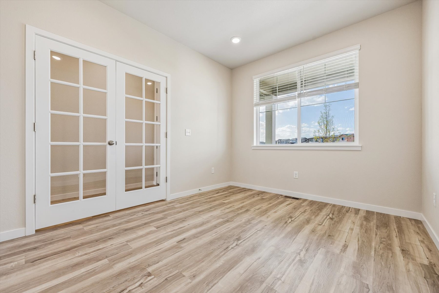 A room with a wood floor and a window with a view of a tree and a building.
