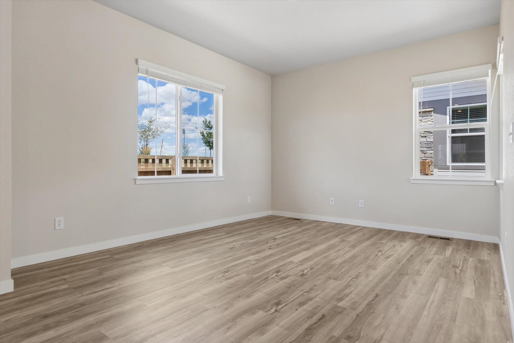 A room with a wood floor and a window with a view of a tree and a building.