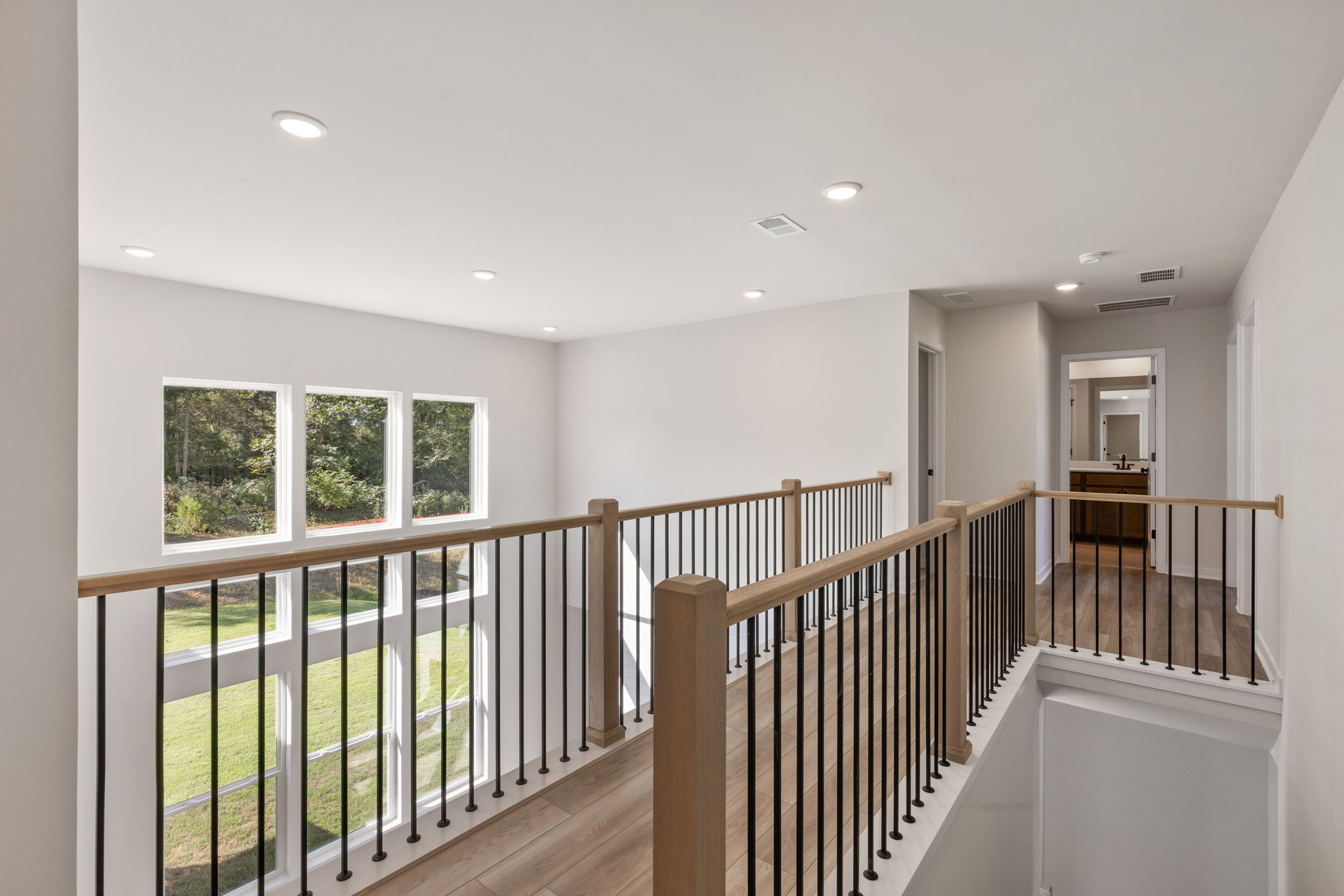 A room with a wood railing and a white wall with windows.