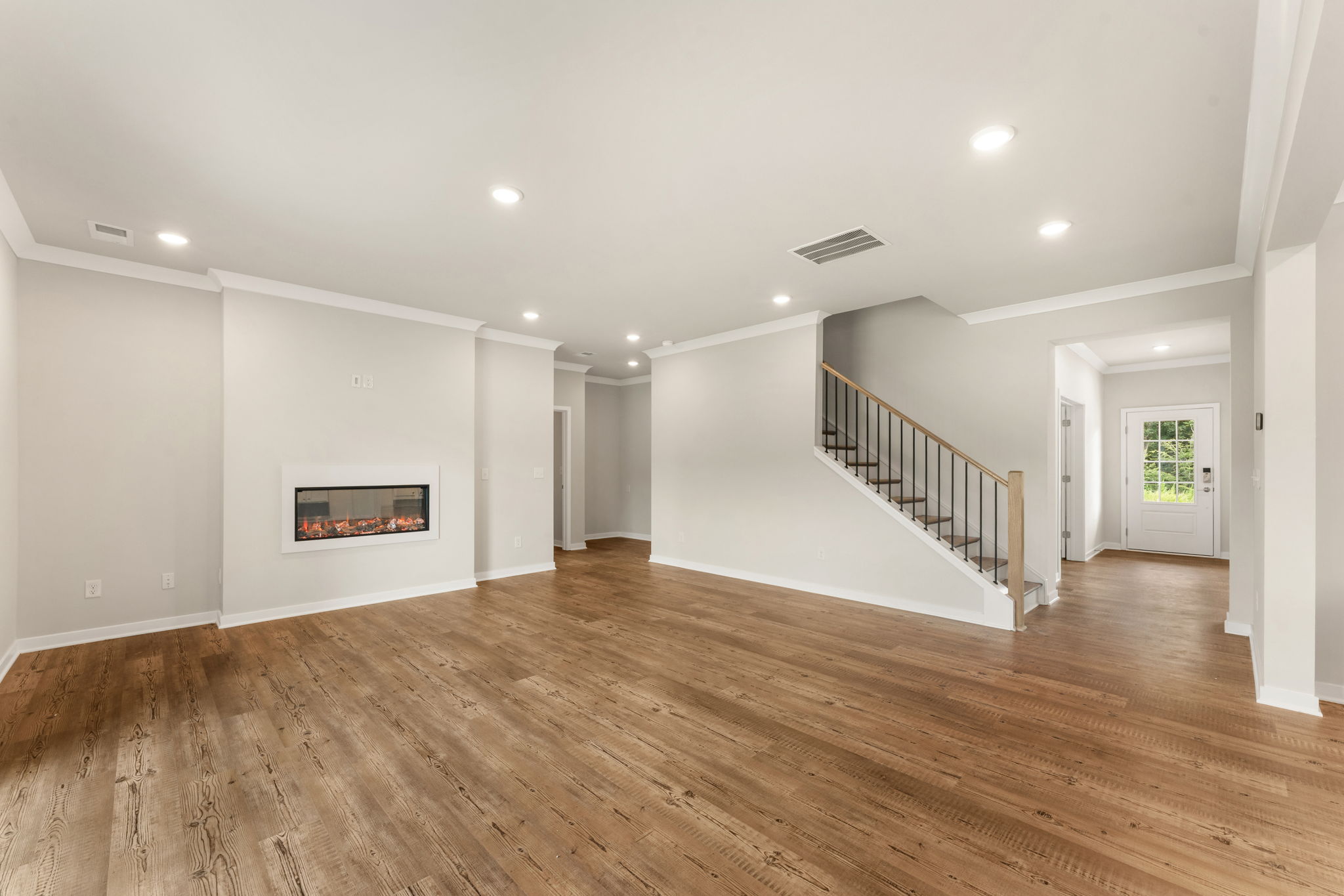 A large empty room with a wood floor and a staircase.
