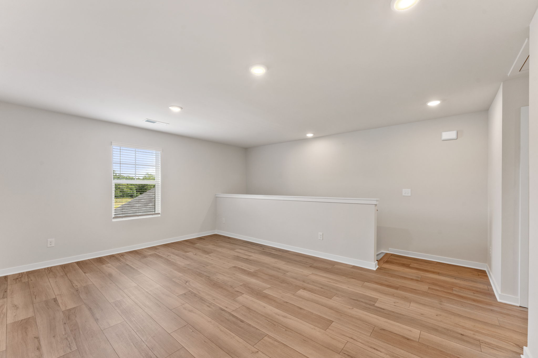 A room with a wood floor and a white wall with a window.