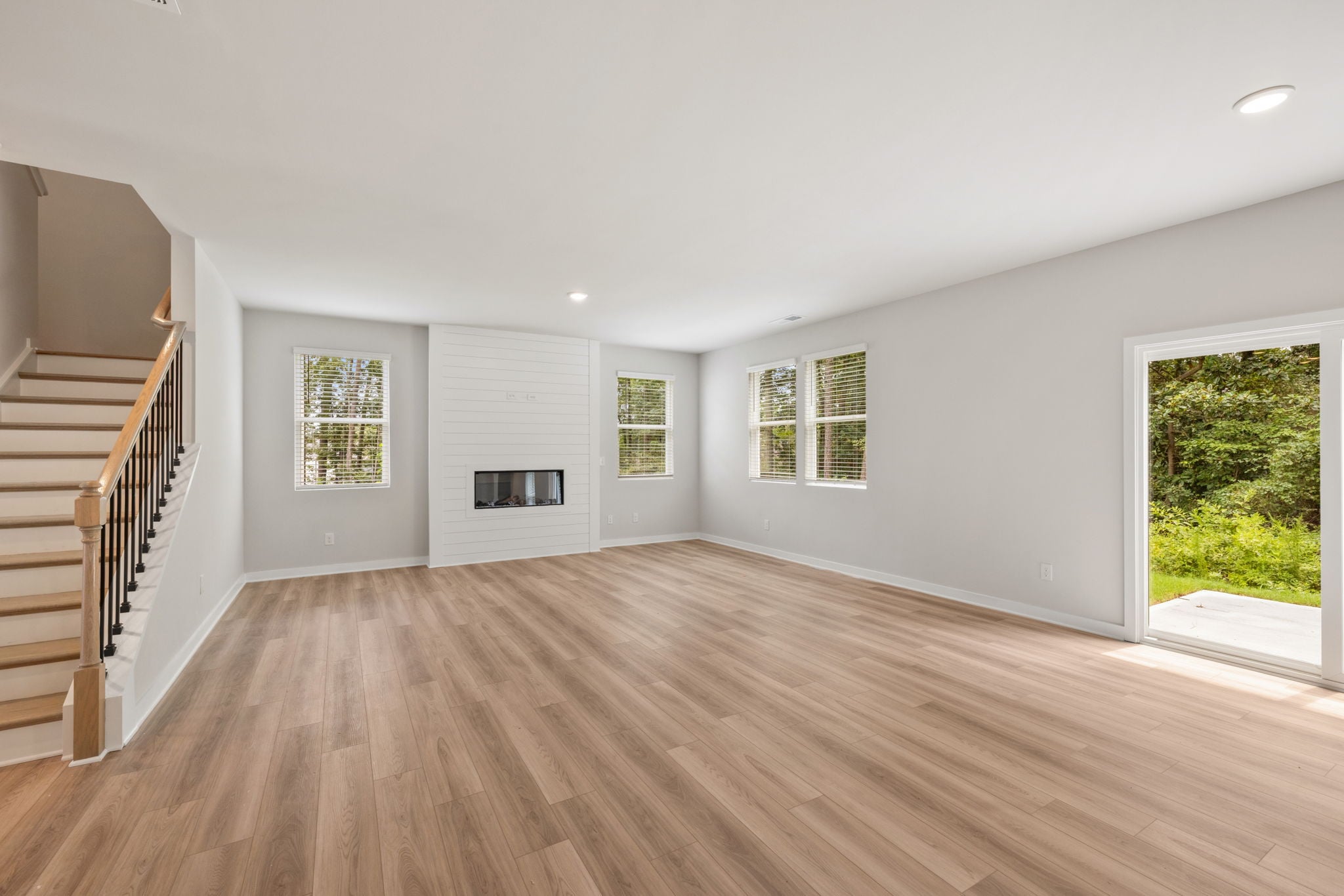 A large empty room with a wood floor and a wood staircase.