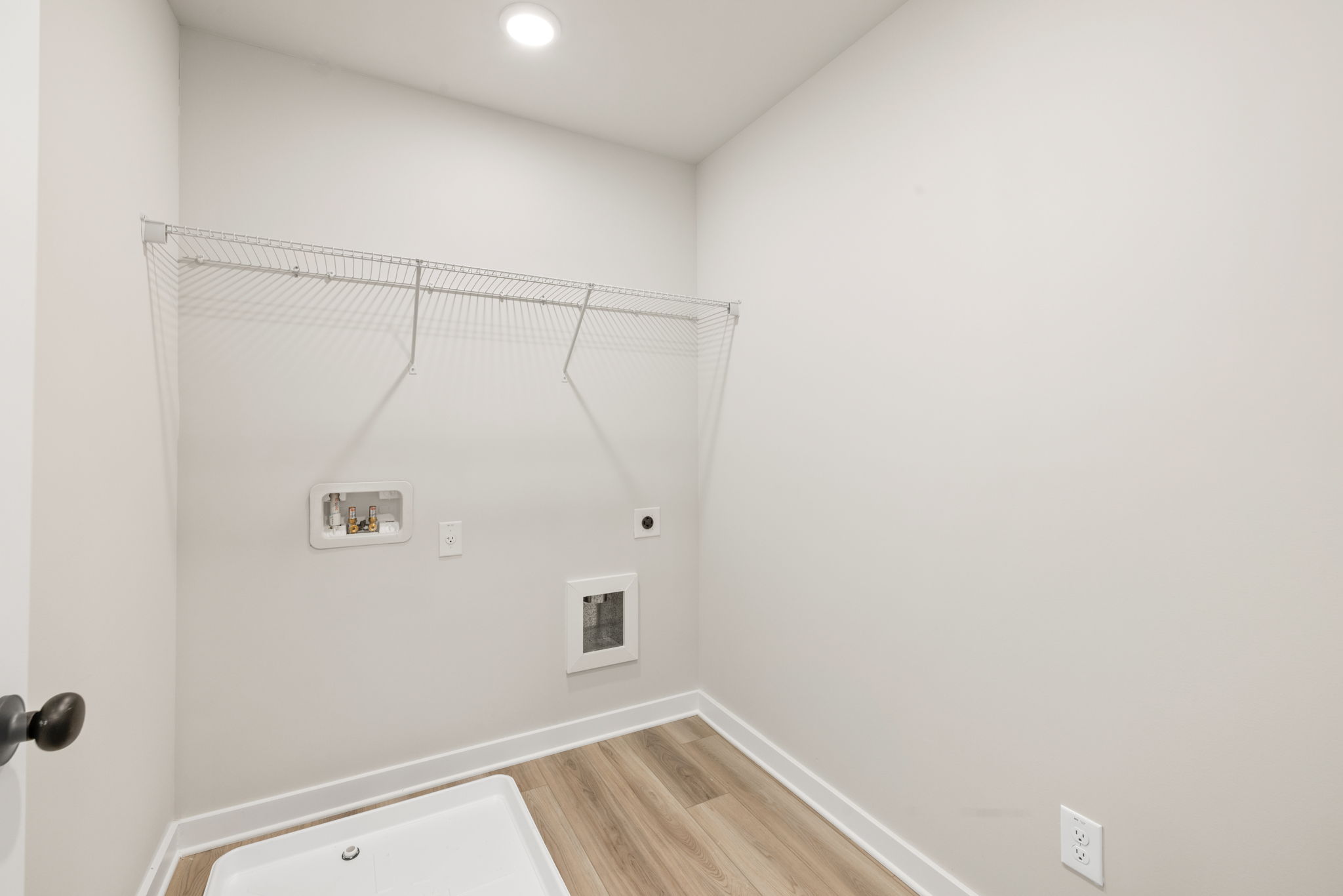 A room with a wood floor and a white wall with a light.