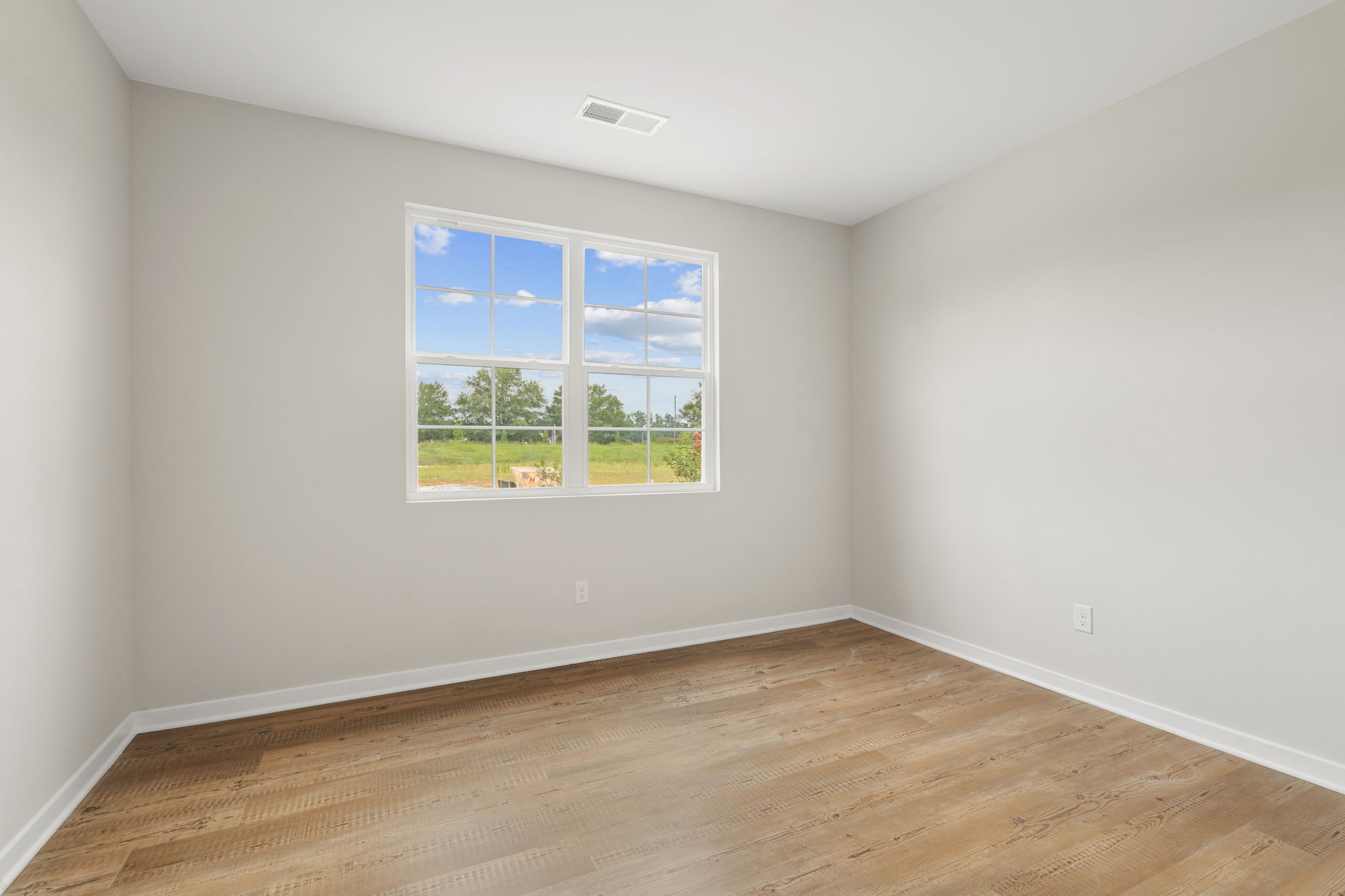 A room with a wood floor and a window with a view of trees.