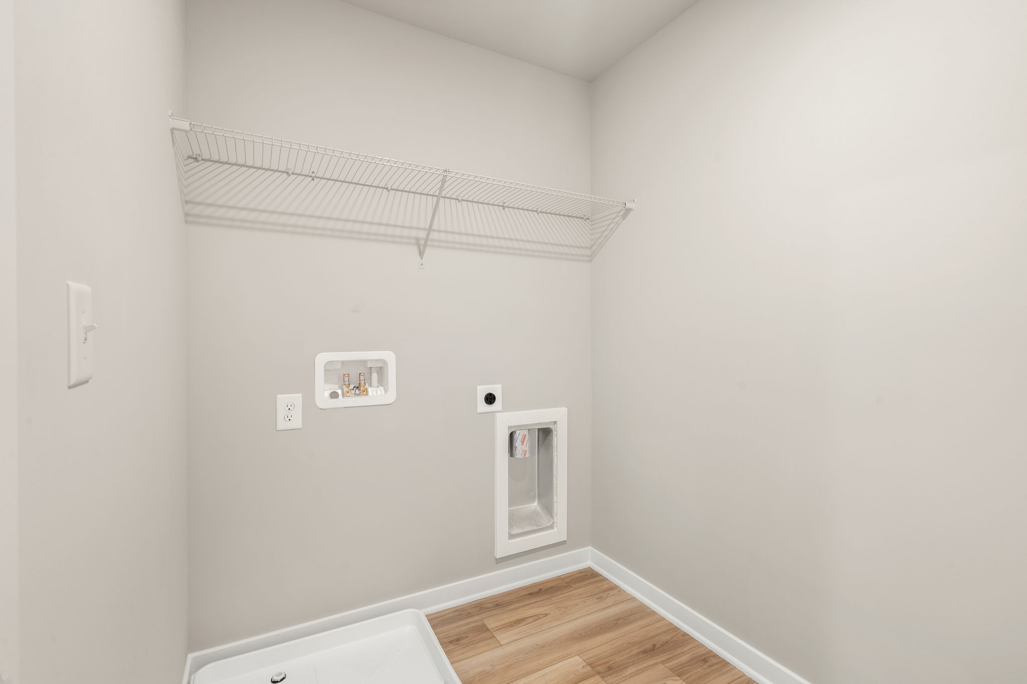 A room with a wood floor and a white wall with a vent.