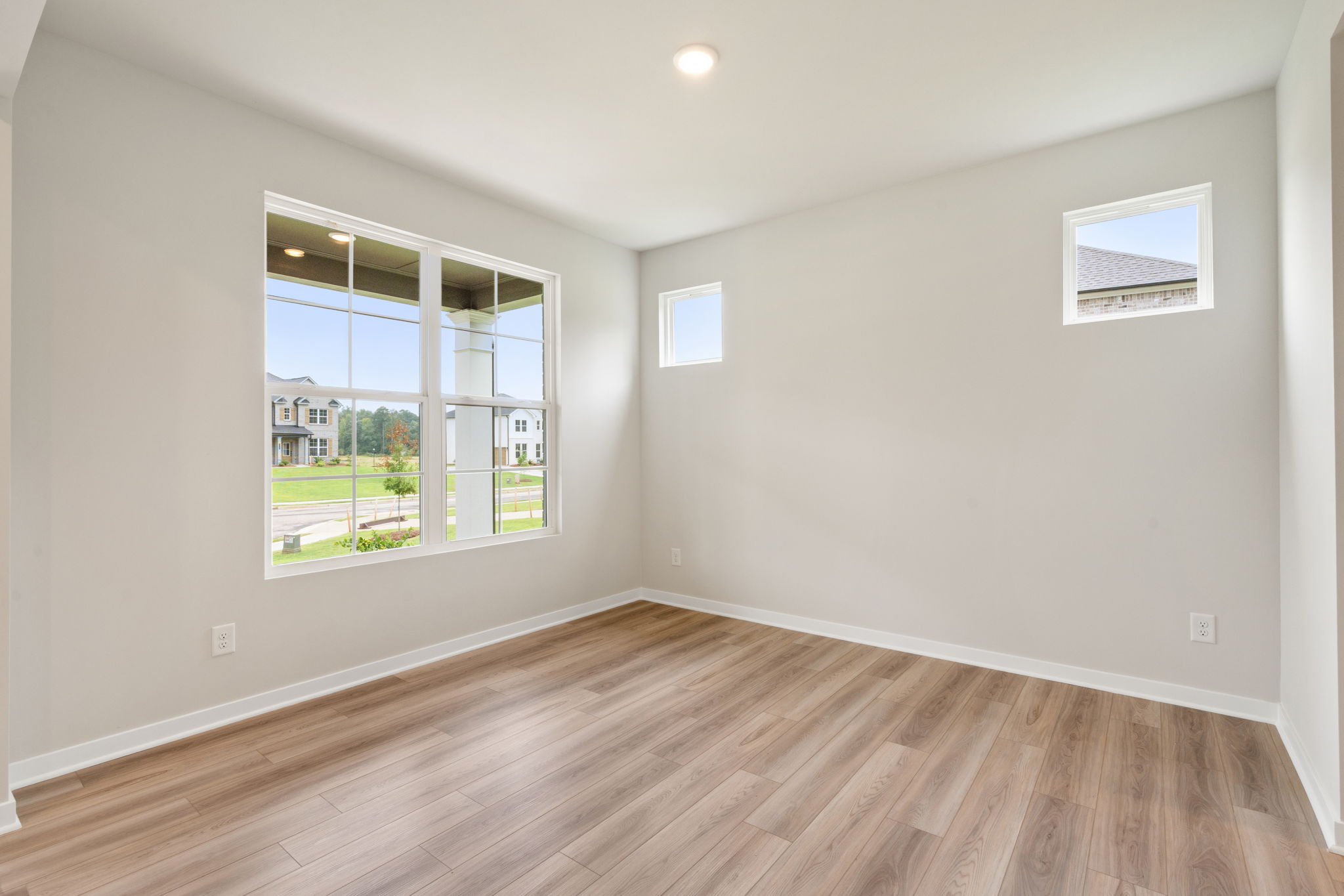 A room with a wood floor and a window with a view of a field and a building.