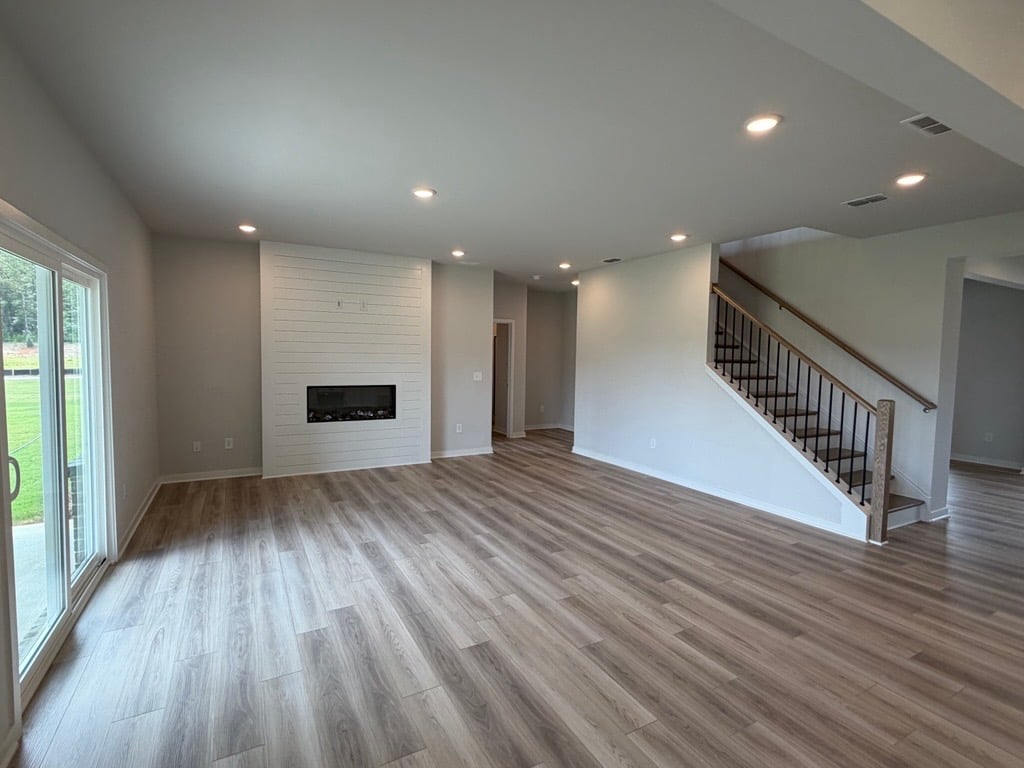 A large empty room with a wood floor and a staircase.