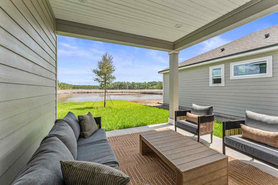 Silverbell II Model Home Covered Patio with Couch and Chairs Overlooking Water at Camden Woods in Kingsland, GA