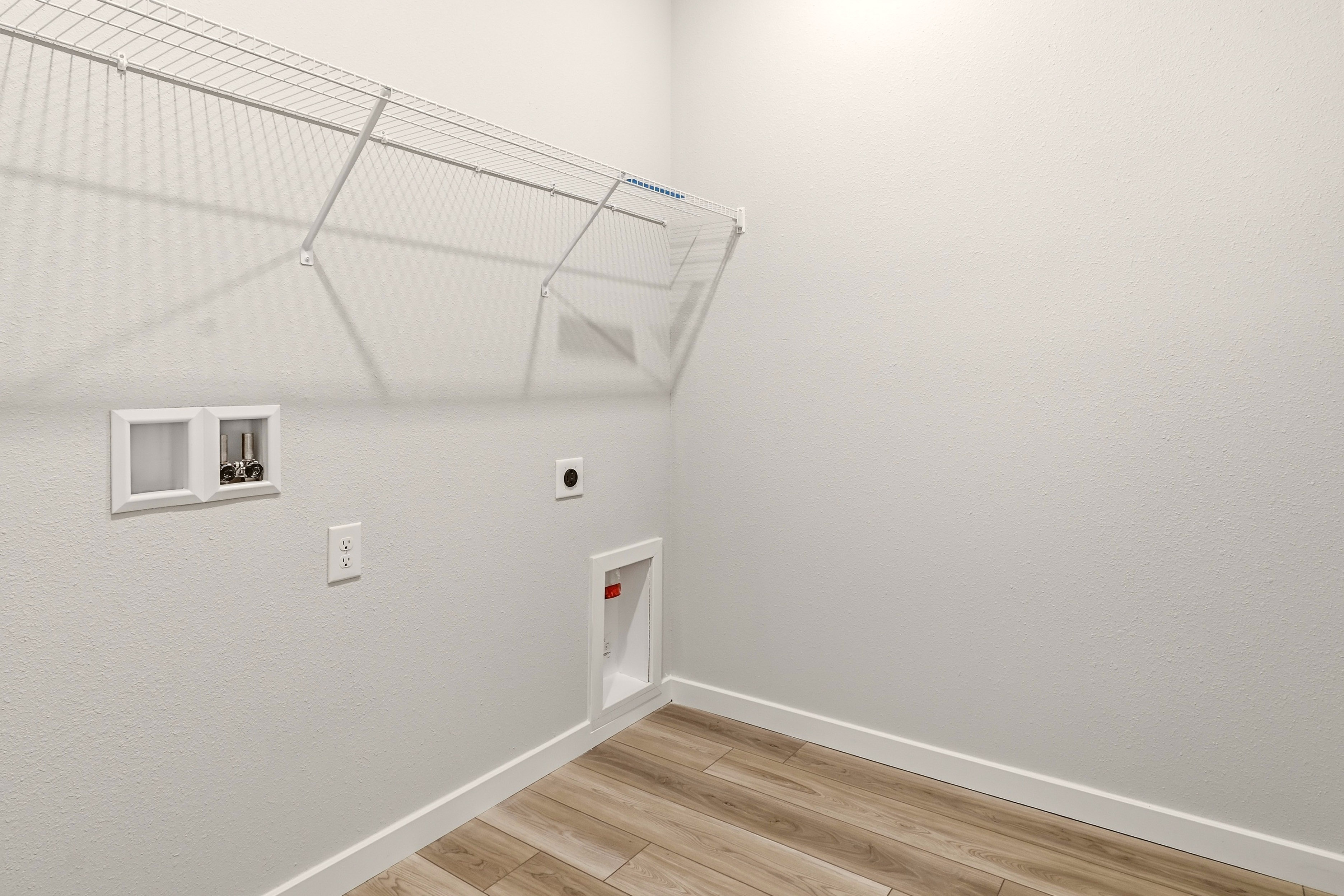 A white room with a wood floor and a white wall with a light.