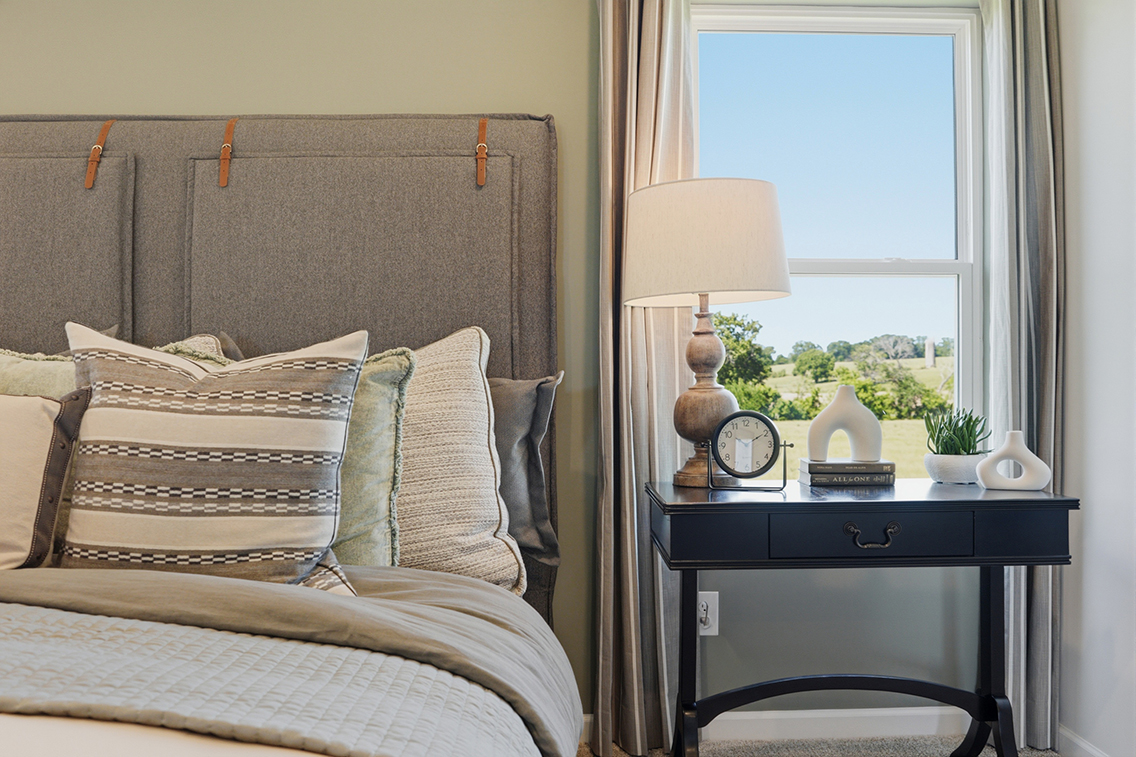 A bed with a lamp and a table with a clock on it.