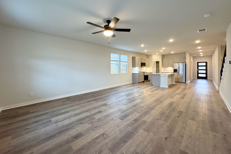 A large empty room with a ceiling fan and a wood floor.