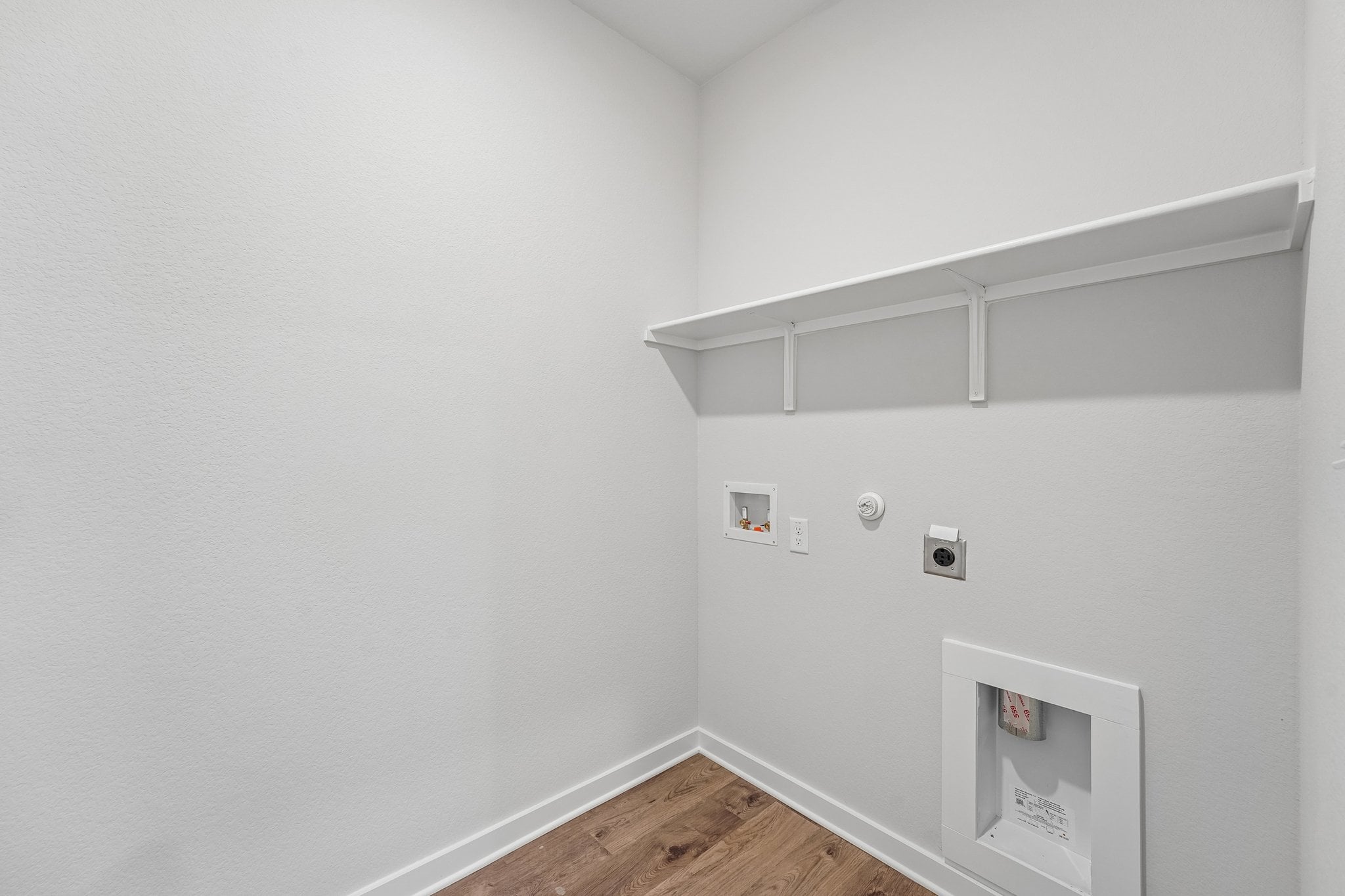 A white wall with a white shelf and a white wall with a white door and a wood floor.