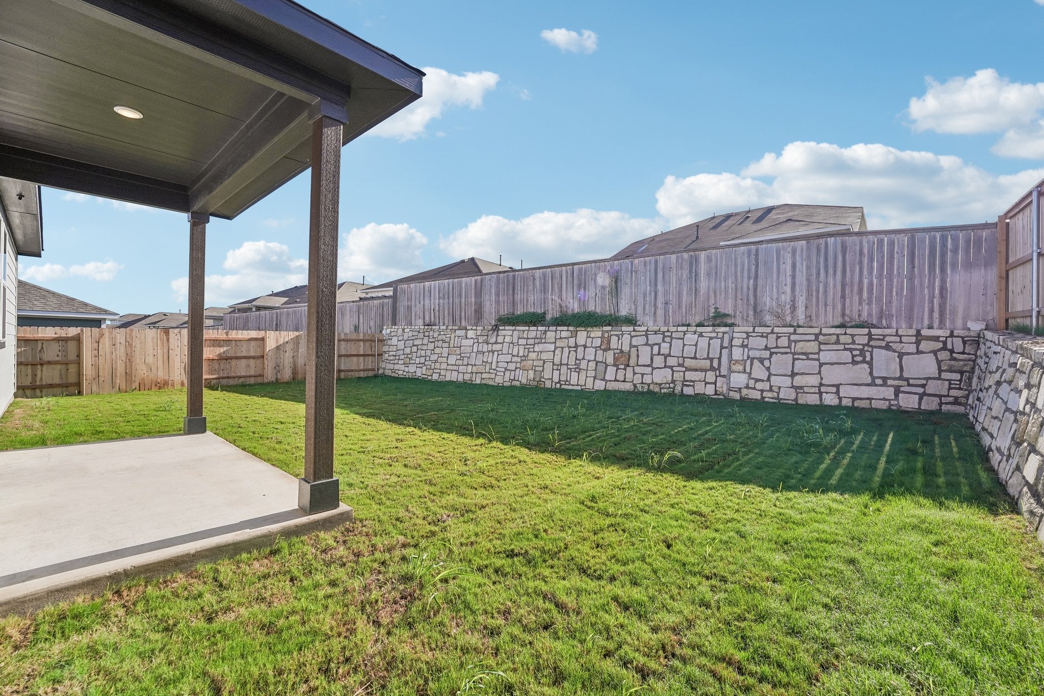 A stone wall with a stone fence and grass and a building.